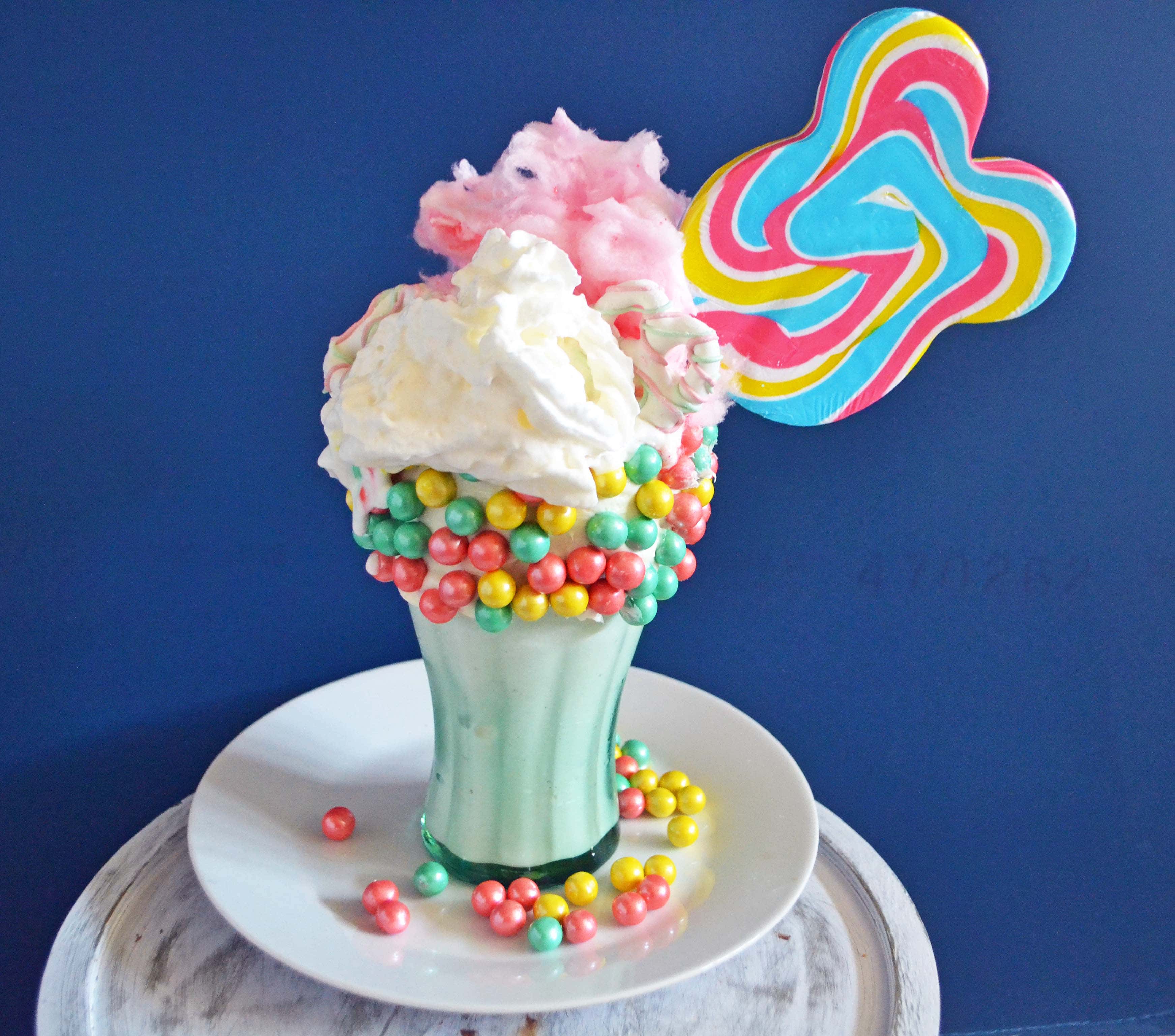 Black Tap Milkshakes Copycat. Cotton Candy Sugar Bomb Milkshake by Modern Honey combines vanilla ice cream, sixlet pastel pearls, cotton candy, white chocolate pretzels, sweet lollipop, and whipped cream.