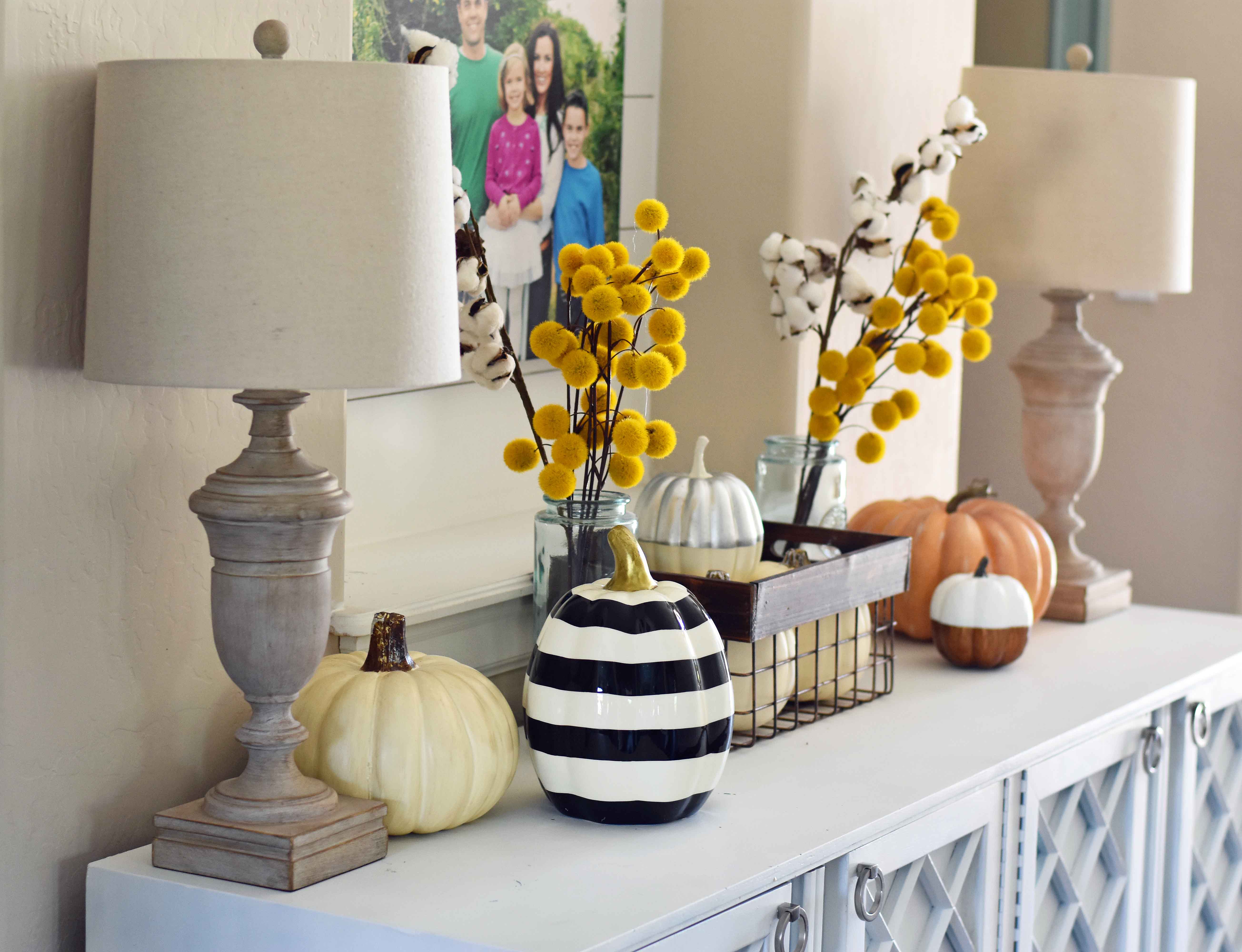 Fall Entry Decor Ideas. Craspedia Yellow Billy Ball Flowers in vintage vases. White pumpkins in wire baskets. Black and white striped pumpkin. Natural lamps, white entry table, and fall decor. Fixer Upper cotton ball stems. How to decorate your home for Fall.