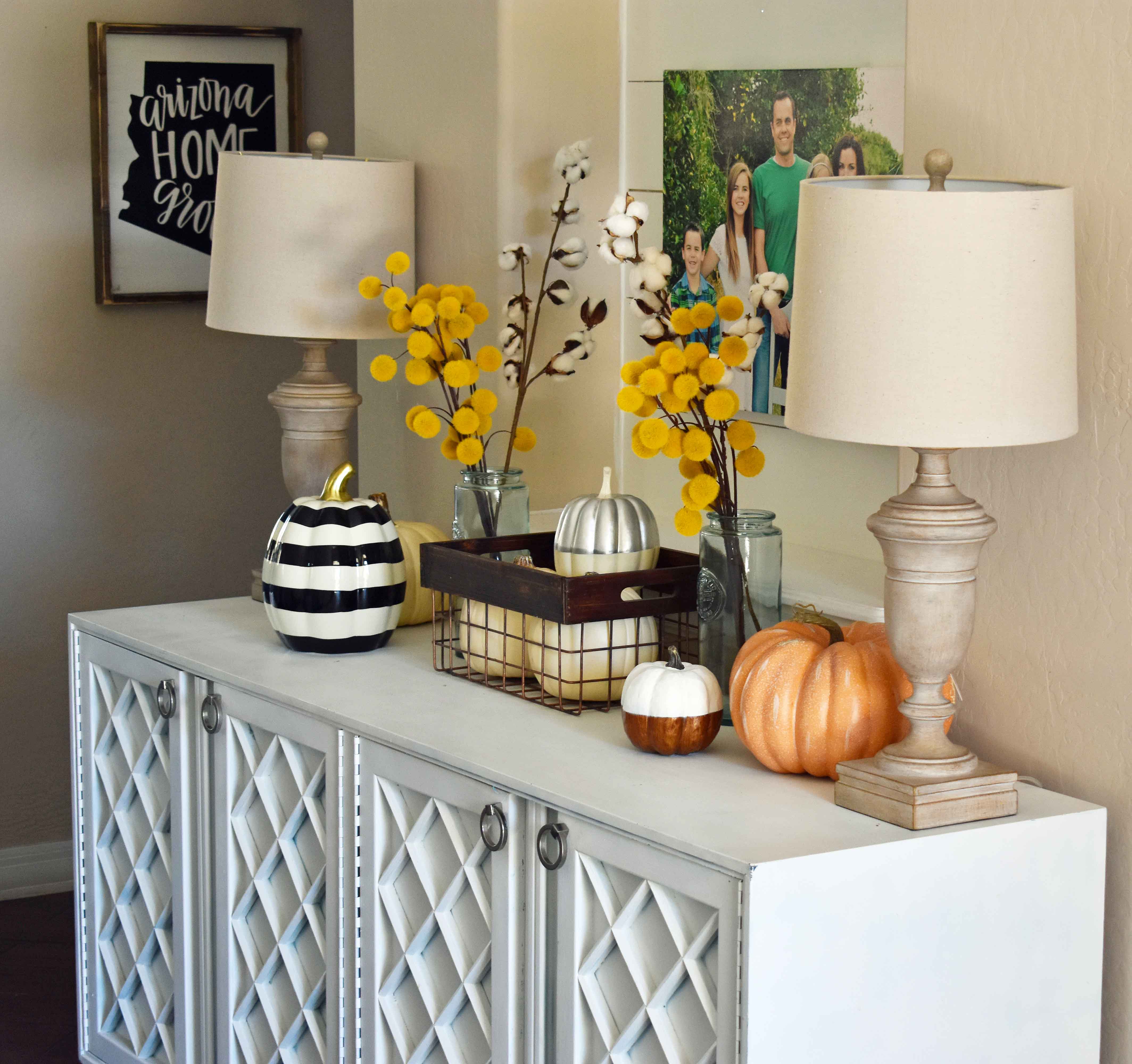 Fall Entry Decor Ideas. Craspedia Yellow Billy Ball Flowers in vintage vases. White pumpkins in wire baskets. Black and white striped pumpkin. Natural lamps, white entry table, and fall decor. Fixer Upper cotton ball stems. How to decorate your home for Fall.