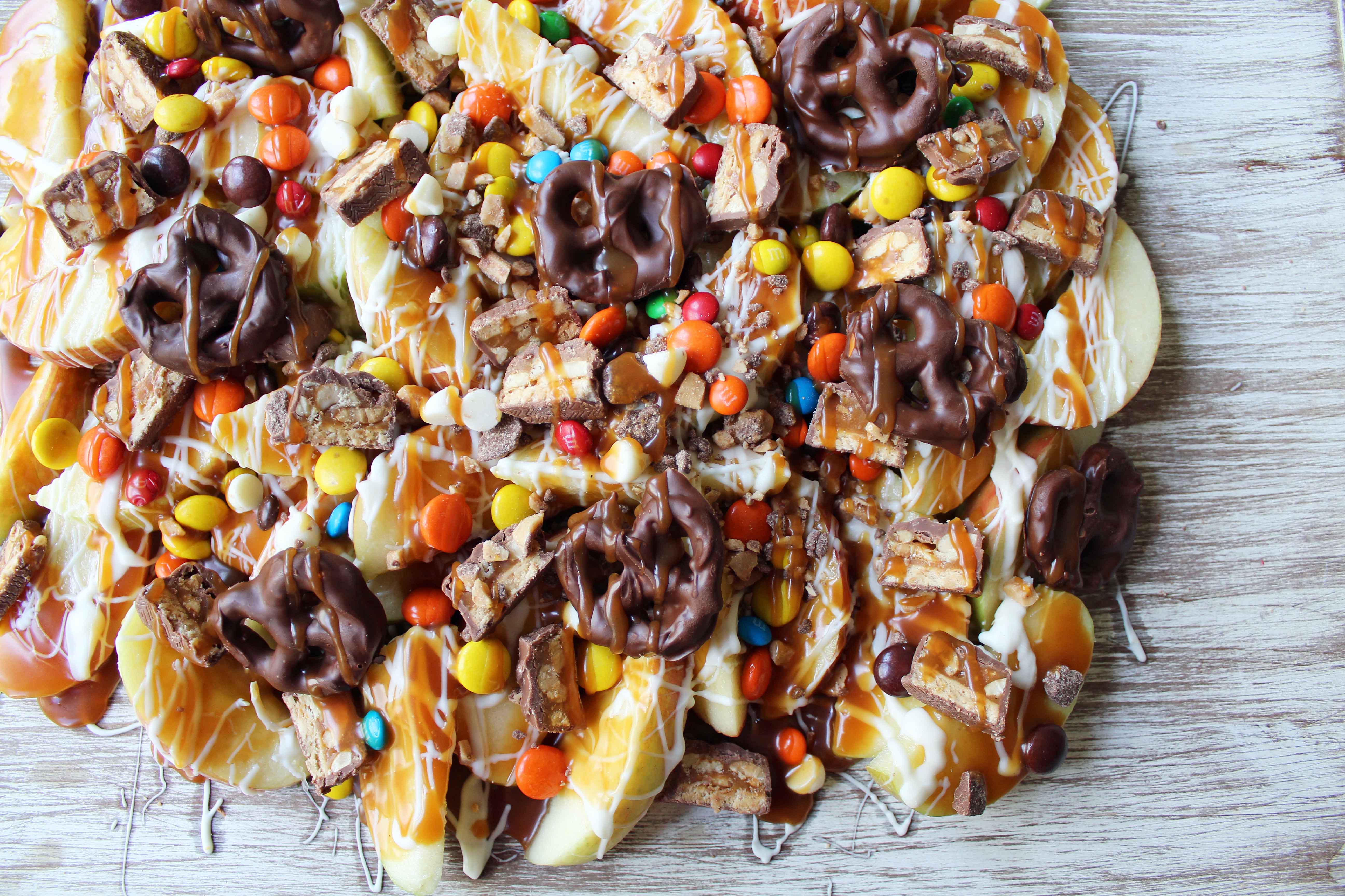 Candy Madness Caramel Apple Nachos by Modern Honey. Crisp Apples topped with Salted Caramel, White Chocolate, M &M's, Reeses Pieces, Heath Toffee Bits, Snickers, and Chocolate Covered Pretzels. These Caramel Apple Nachos are much easier than making caramel apples and will be a huge hit at your next party!