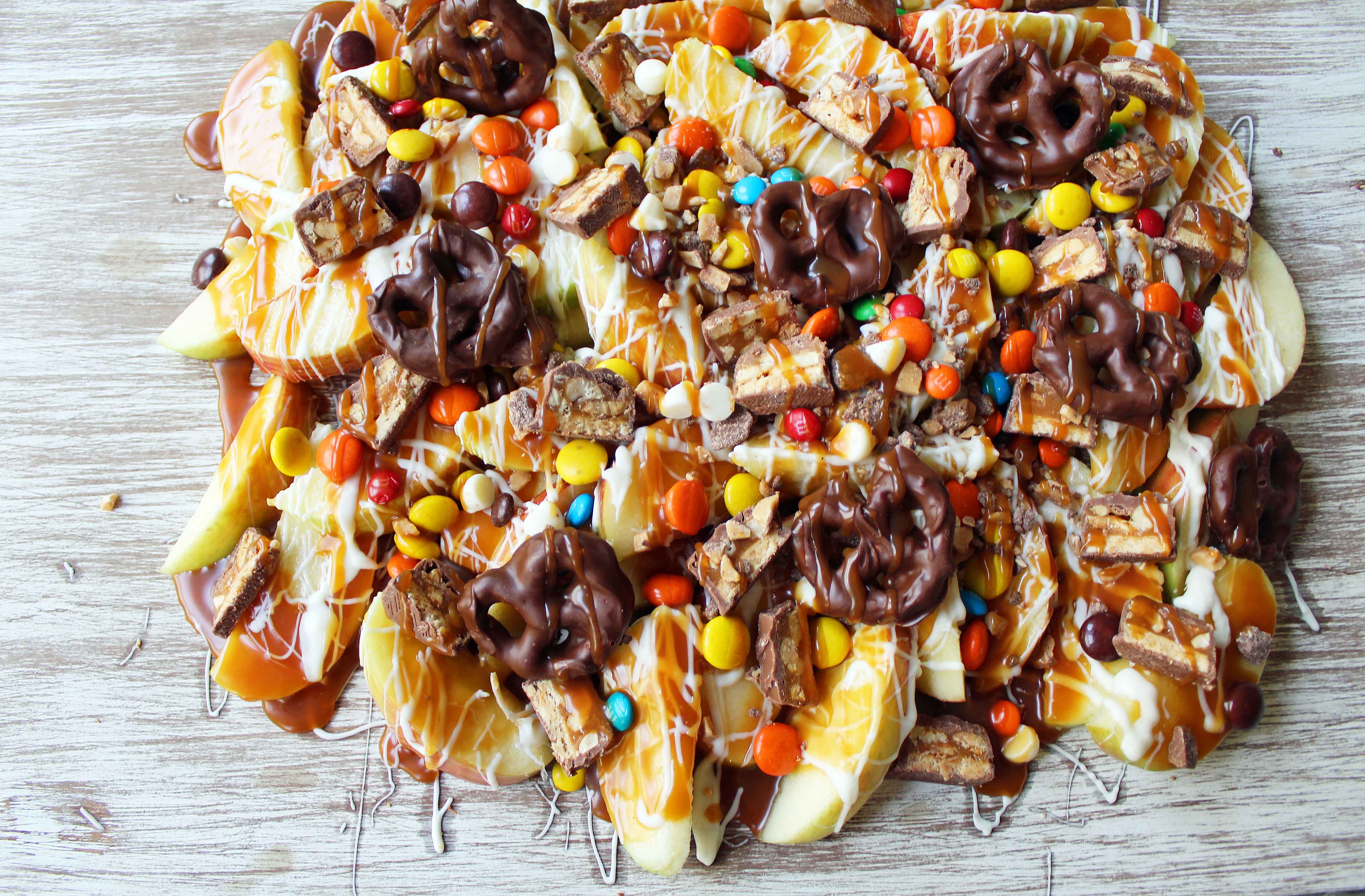 Candy Madness Caramel Apple Nachos by Modern Honey. Crisp Apples topped with Salted Caramel, White Chocolate, M &M's, Reeses Pieces, Heath Toffee Bits, Snickers, and Chocolate Covered Pretzels. These Caramel Apple Nachos are much easier than making caramel apples and will be a huge hit at your next party!