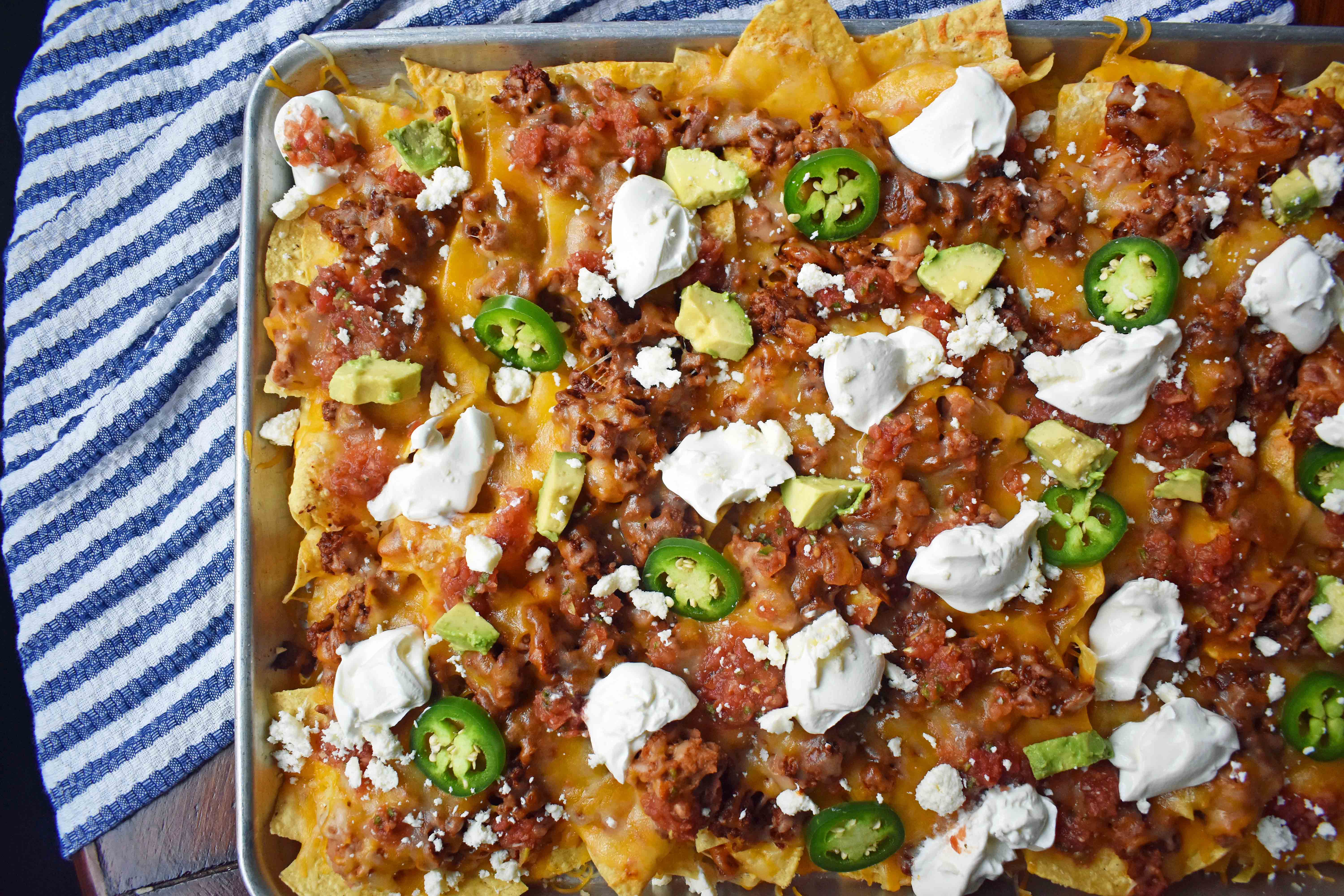 Ultimate Spicy Beef Nachos by Modern Honey. Layers of spicy beef, refried beans, mexican cheese, sour cream, avocado, and jalapenos. These are the perfect party snack for your next party!