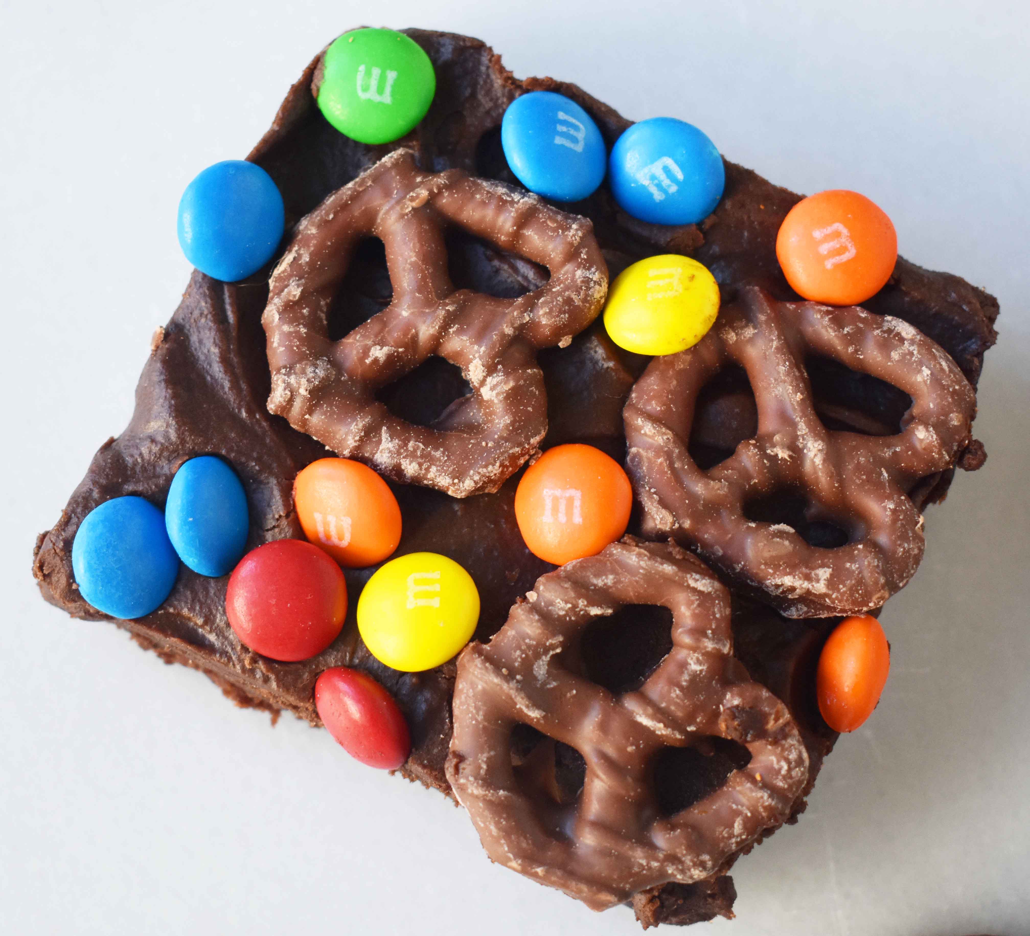 Super Bowl Chocolate Covered Pretzel Brownies. Chewy rich chocolate chunk brownies topped with creamy frosting, chocolate covered pretzels, and M & M's. www.modernhoney.com