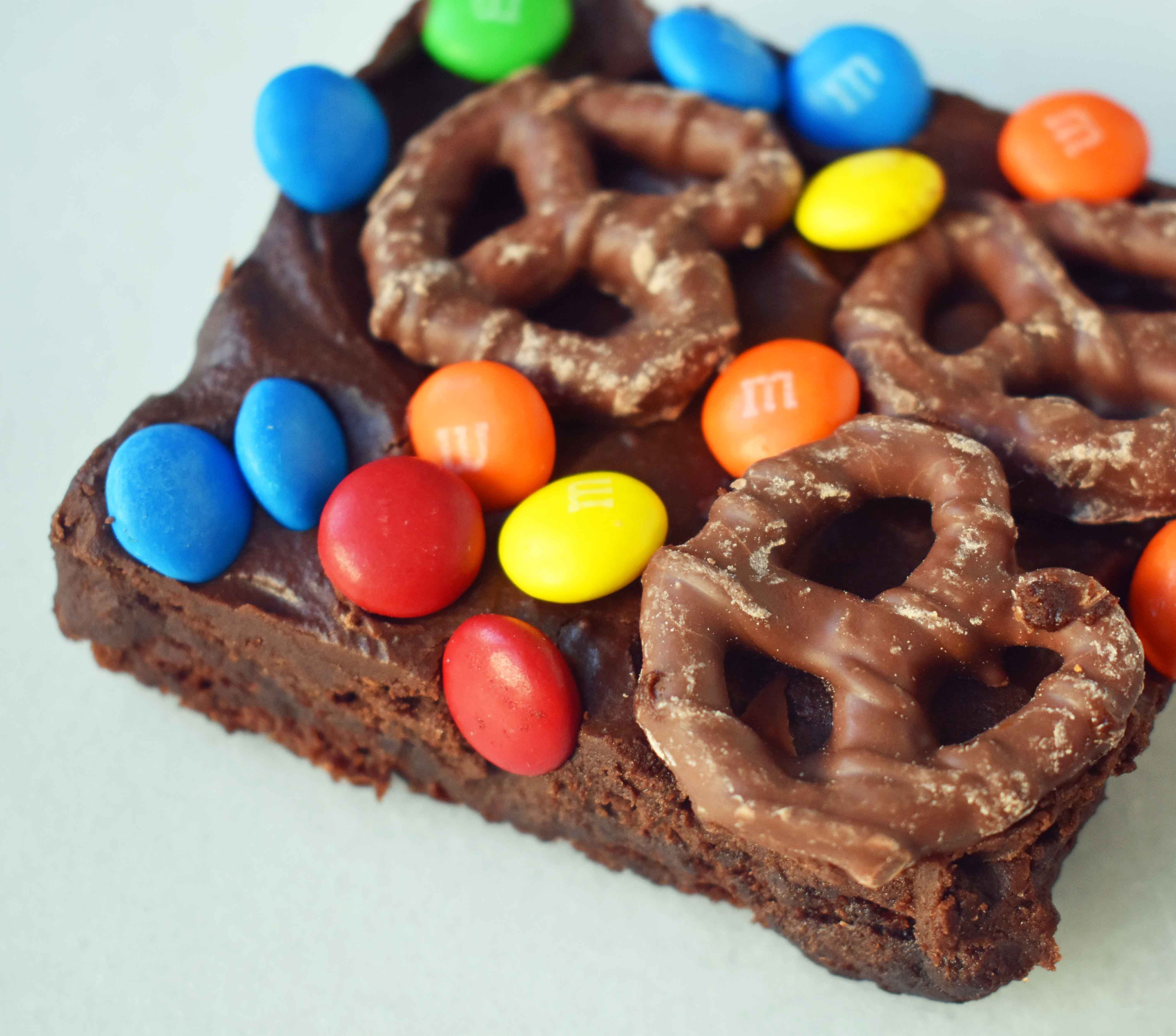 Super Bowl Chocolate Covered Pretzel Brownies. Chewy rich chocolate chunk brownies topped with creamy frosting, chocolate covered pretzels, and M & M's. www.modernhoney.com