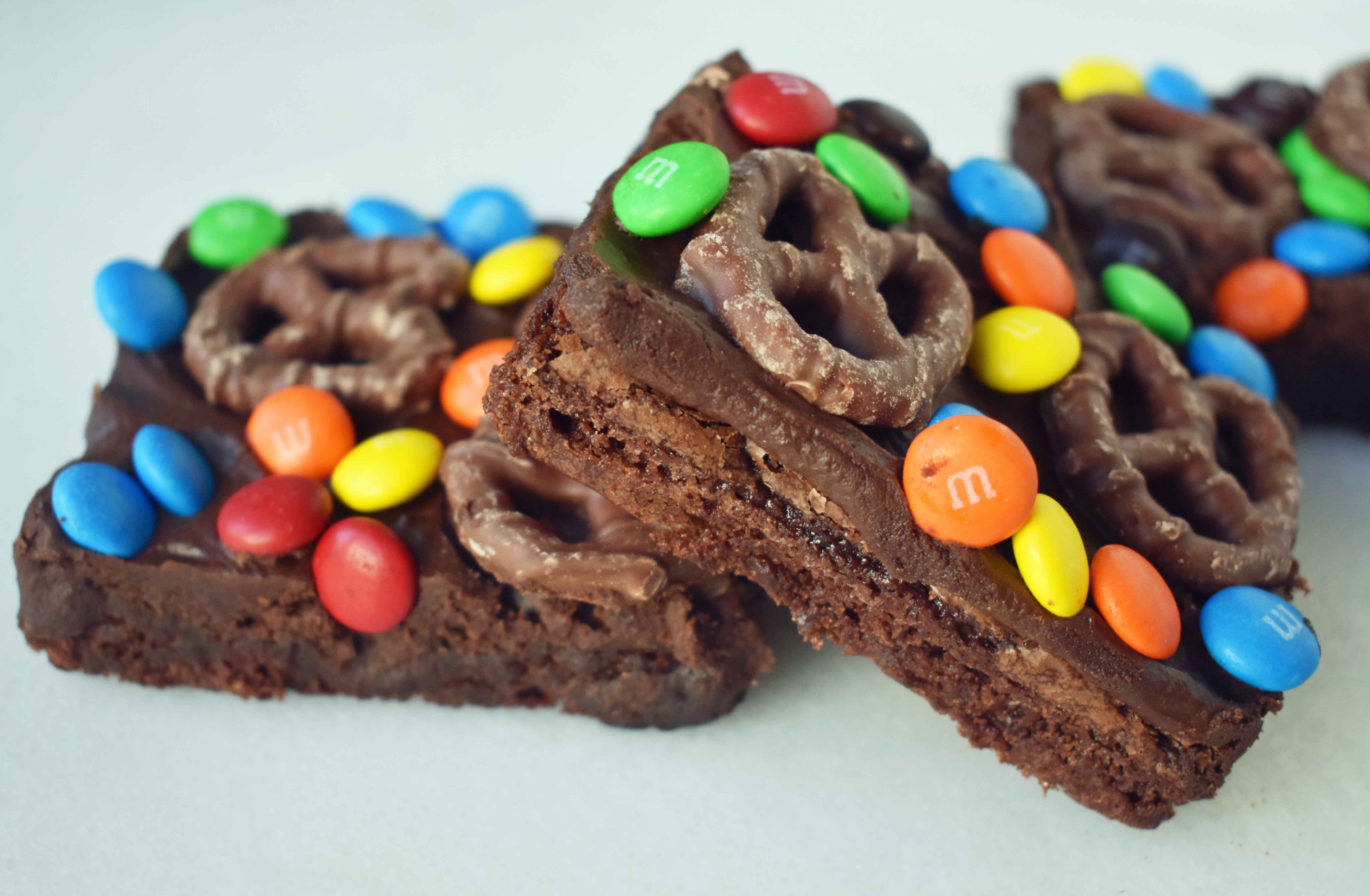 Super Bowl Chocolate Covered Pretzel Brownies. Chewy rich chocolate chunk brownies topped with creamy frosting, chocolate covered pretzels, and M & M's. www.modernhoney.com