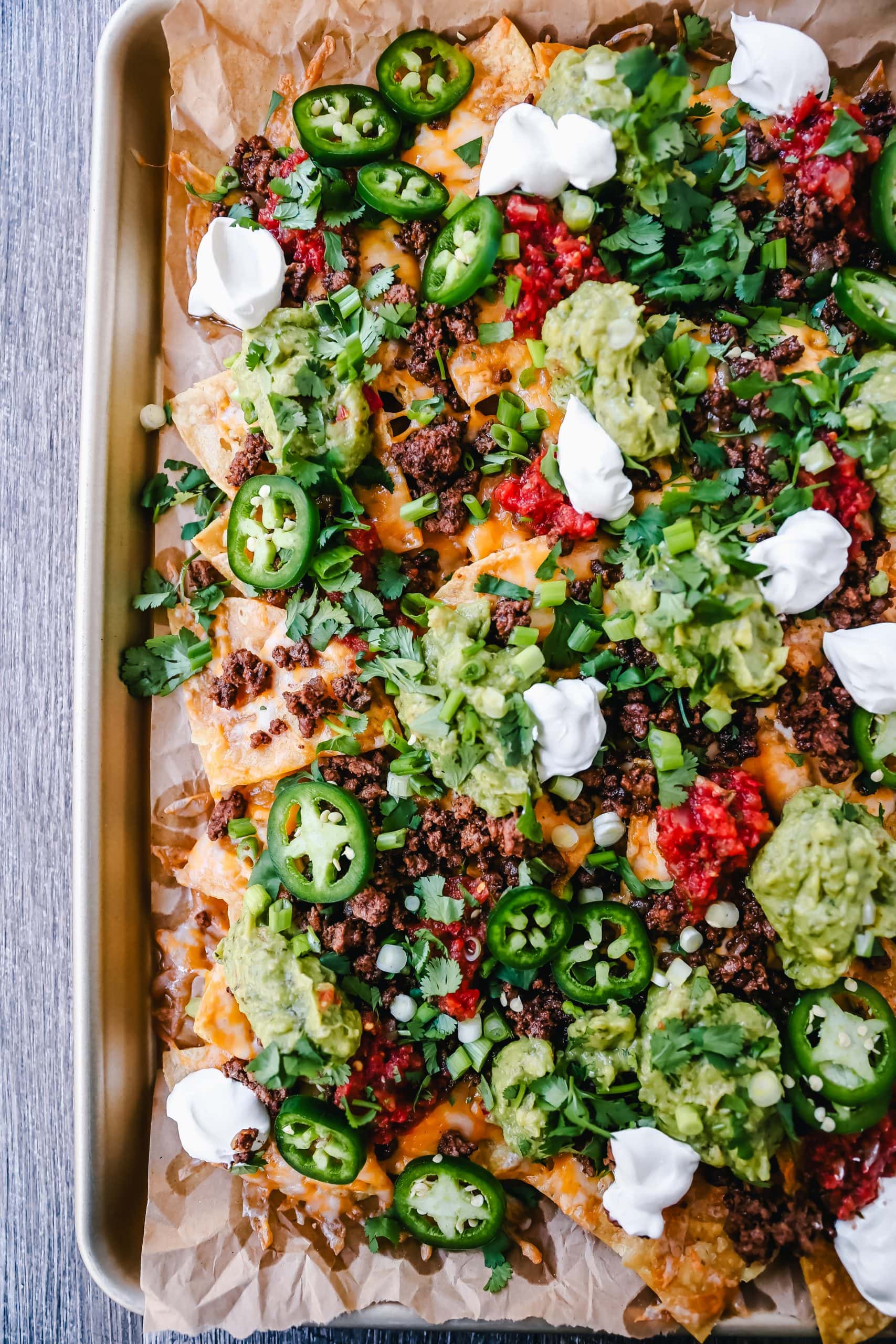 Ground Beef Nachos Recipe  Seasoned ground beef with crispy tortilla chips, Mexican cheeses, fresh guacamole, sour cream, jalapenos, fresh salsa, green onions, and cilantro make the best beef nachos!