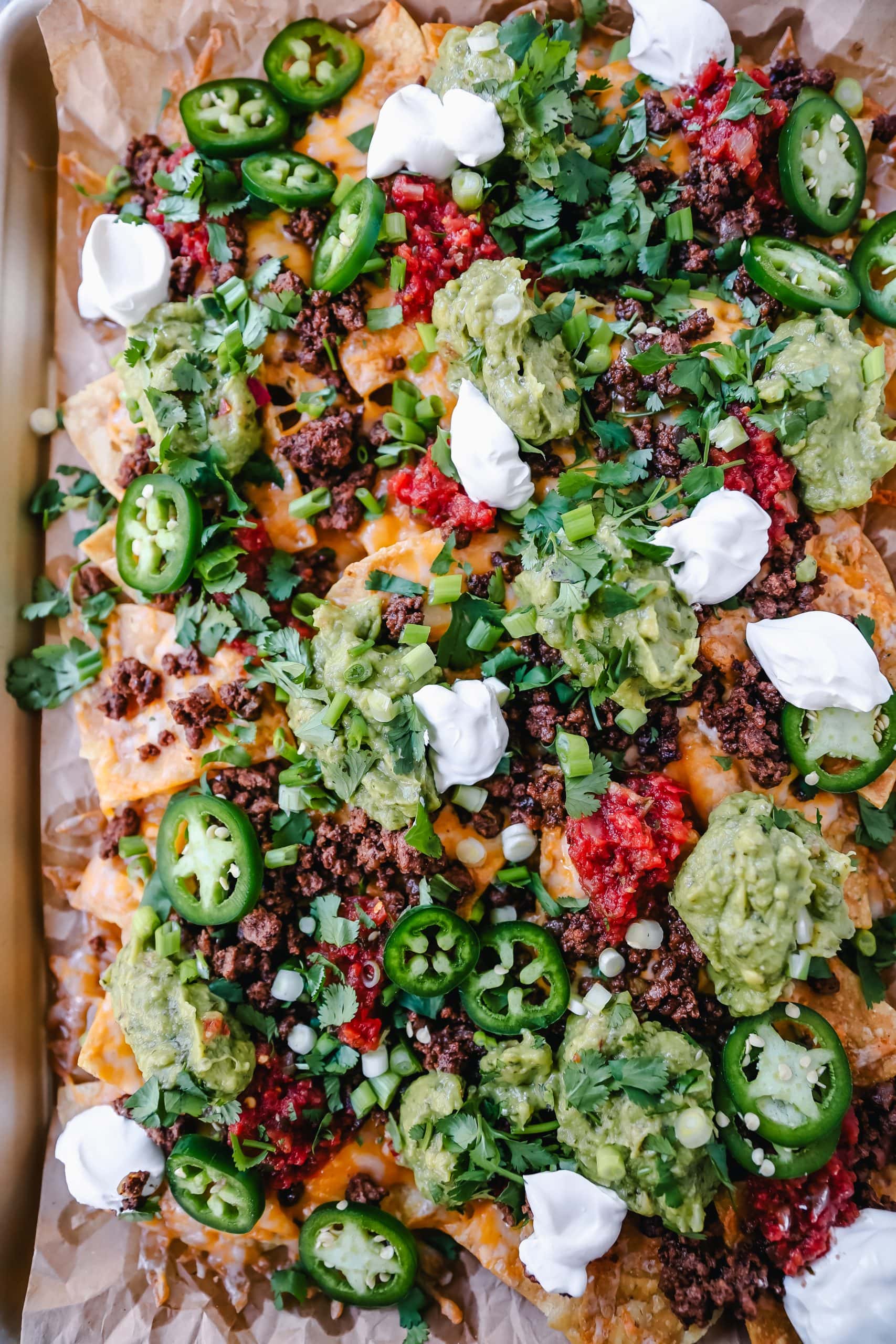 Ground Beef Nachos Recipe  Seasoned ground beef with crispy tortilla chips, Mexican cheeses, fresh guacamole, sour cream, jalapenos, fresh salsa, green onions, and cilantro make the best beef nachos!