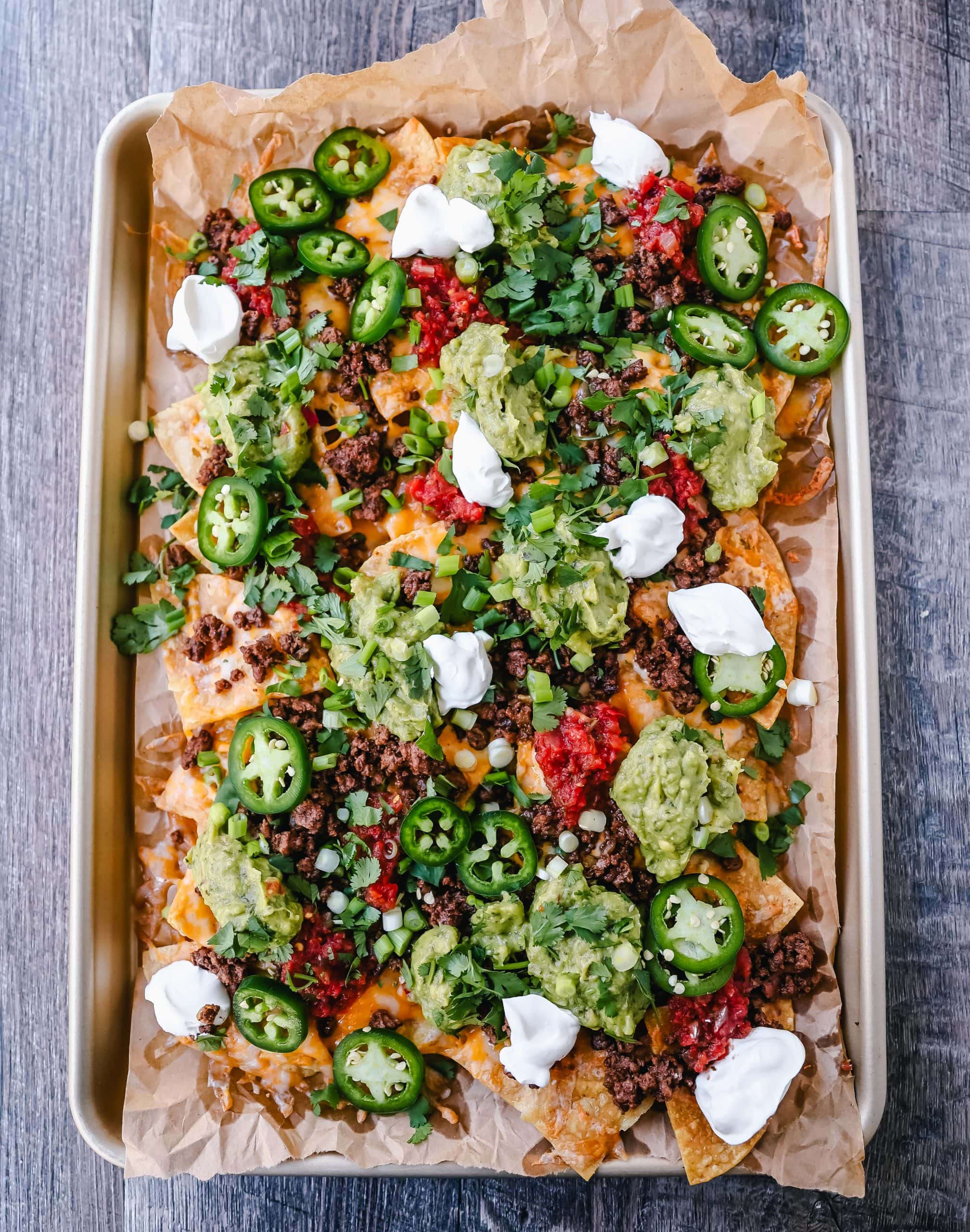 Ground Beef Nachos Recipe  Seasoned ground beef with crispy tortilla chips, Mexican cheeses, fresh guacamole, sour cream, jalapenos, fresh salsa, green onions, and cilantro make the best beef nachos!