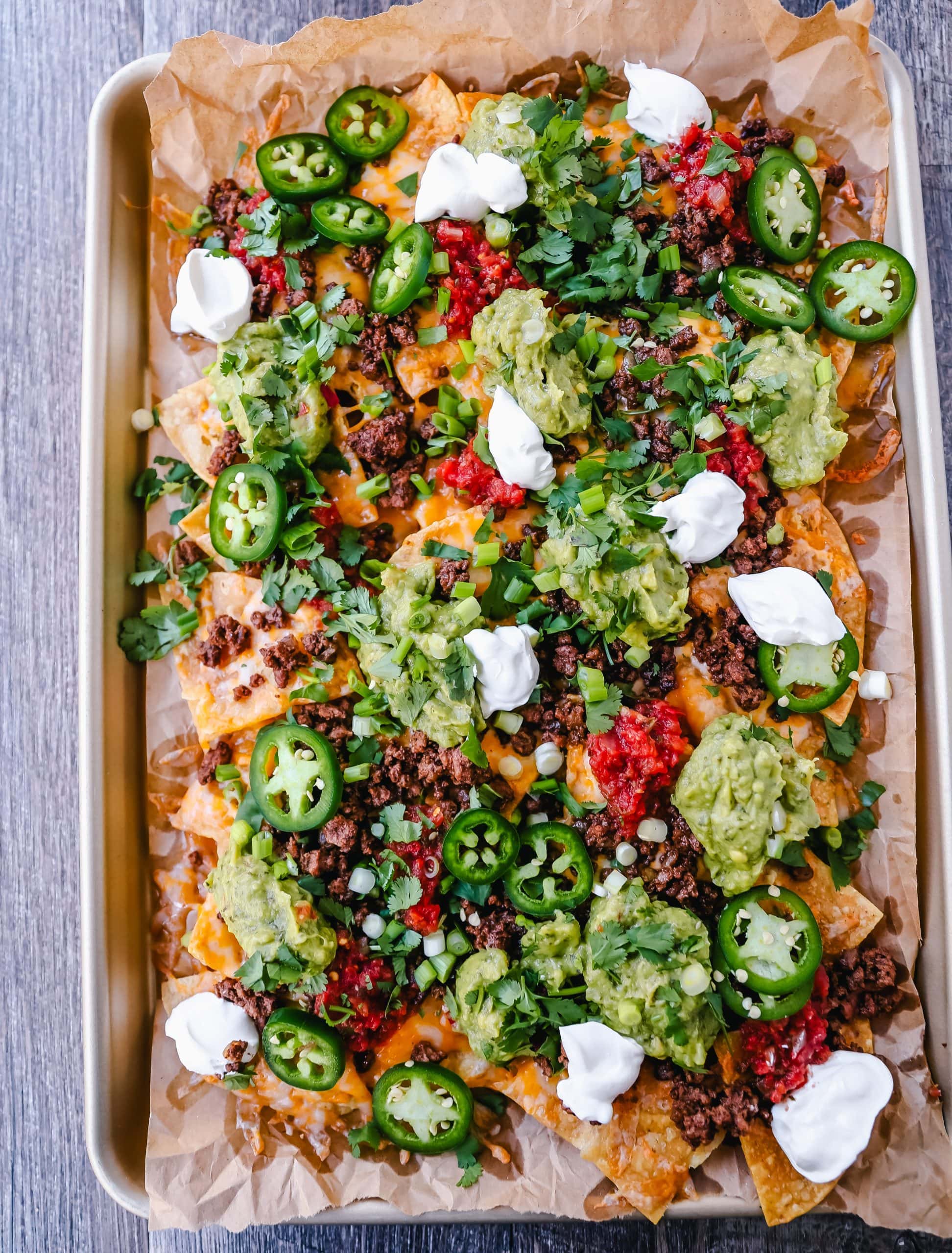 Ground Beef Nachos Recipe  Seasoned ground beef with crispy tortilla chips, Mexican cheeses, fresh guacamole, sour cream, jalapenos, fresh salsa, green onions, and cilantro make the best beef nachos!