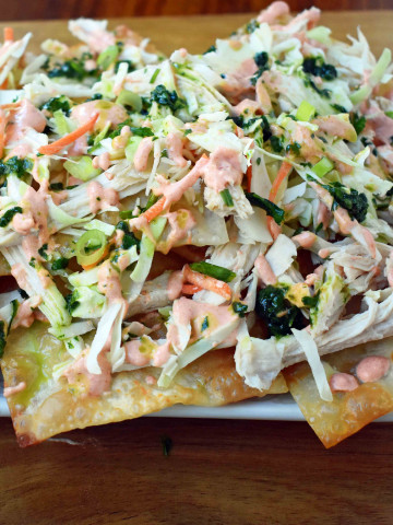 Asian Wonton Chicken Nachos. Fried wontons, pulled chicken, sriracha cream, cabbage mix, and sweet cilantro sauce. An Asian twist on nachos for the perfect party appetizer.