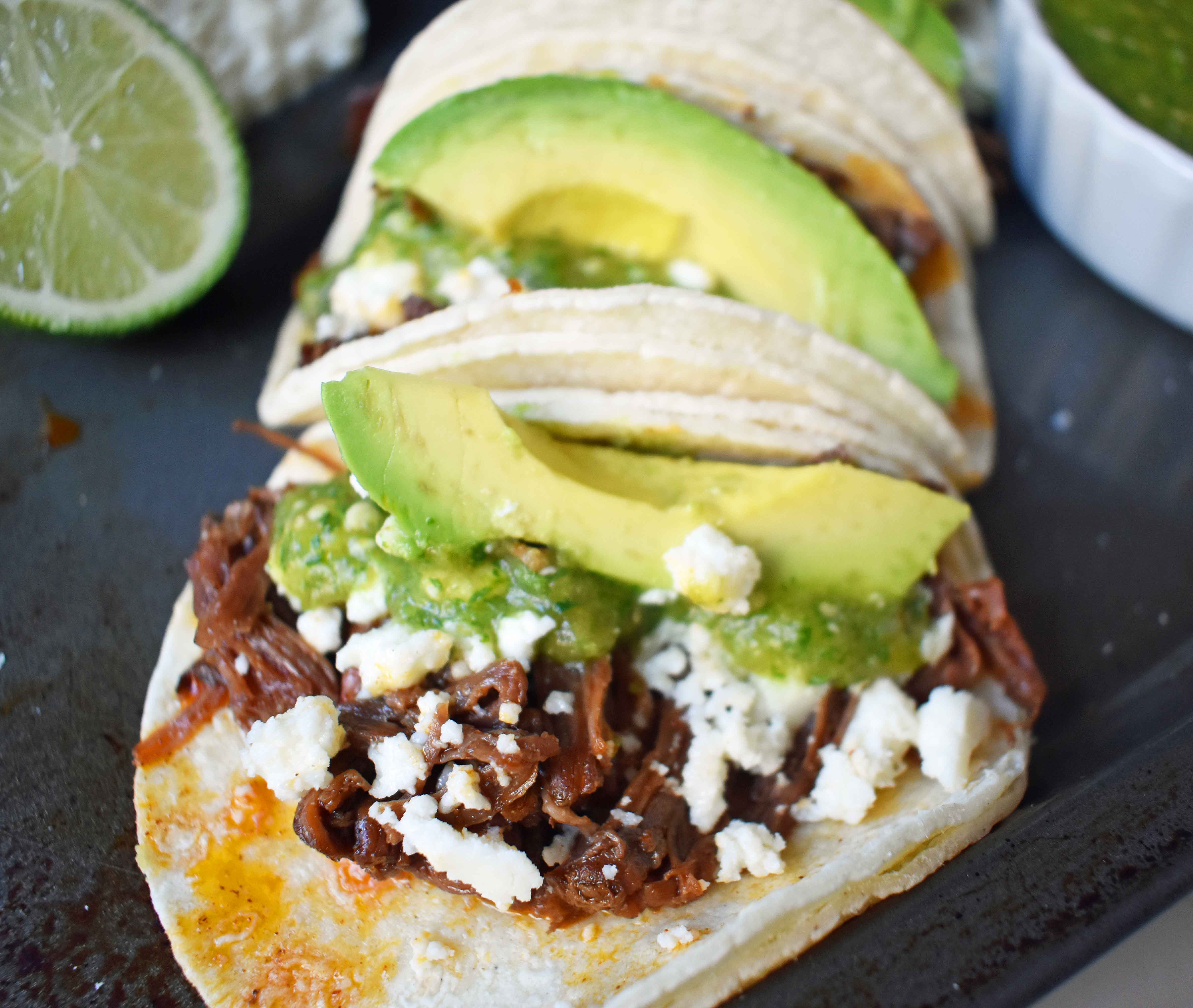Slow Cooker Beef Barbacoa Tacos with Homemade Tomatillo Salsa. Tender spicy beef barbacoa made in slow cooker and topped with fresh avocado, queso fresco cheese, and homemade tomatillo salsa. www.modernhoney.com