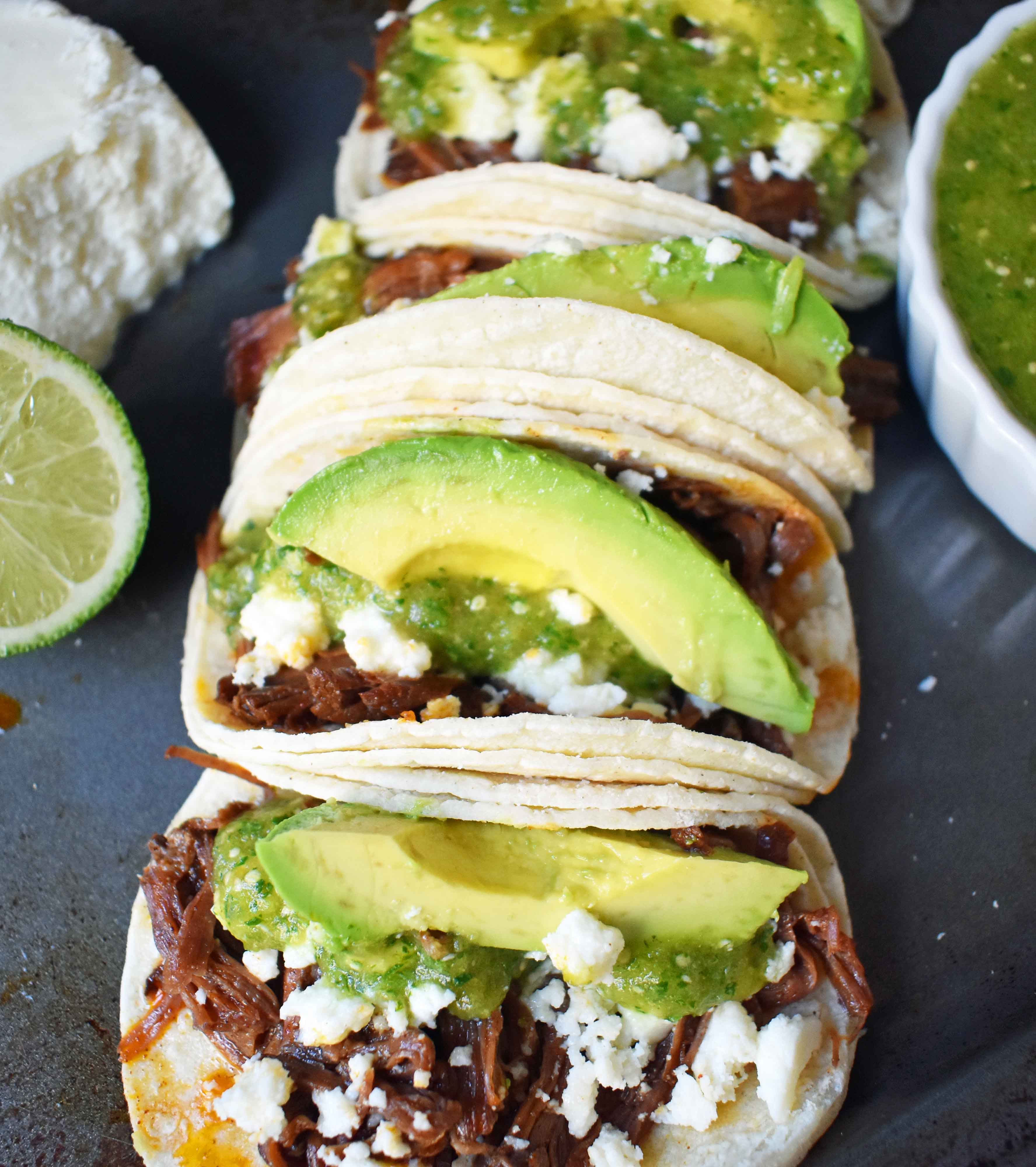 Slow Cooker Beef Barbacoa Tacos with Homemade Tomatillo Salsa. Tender spicy beef barbacoa made in slow cooker and topped with fresh avocado, queso fresco cheese, and homemade tomatillo salsa. www.modernhoney.com