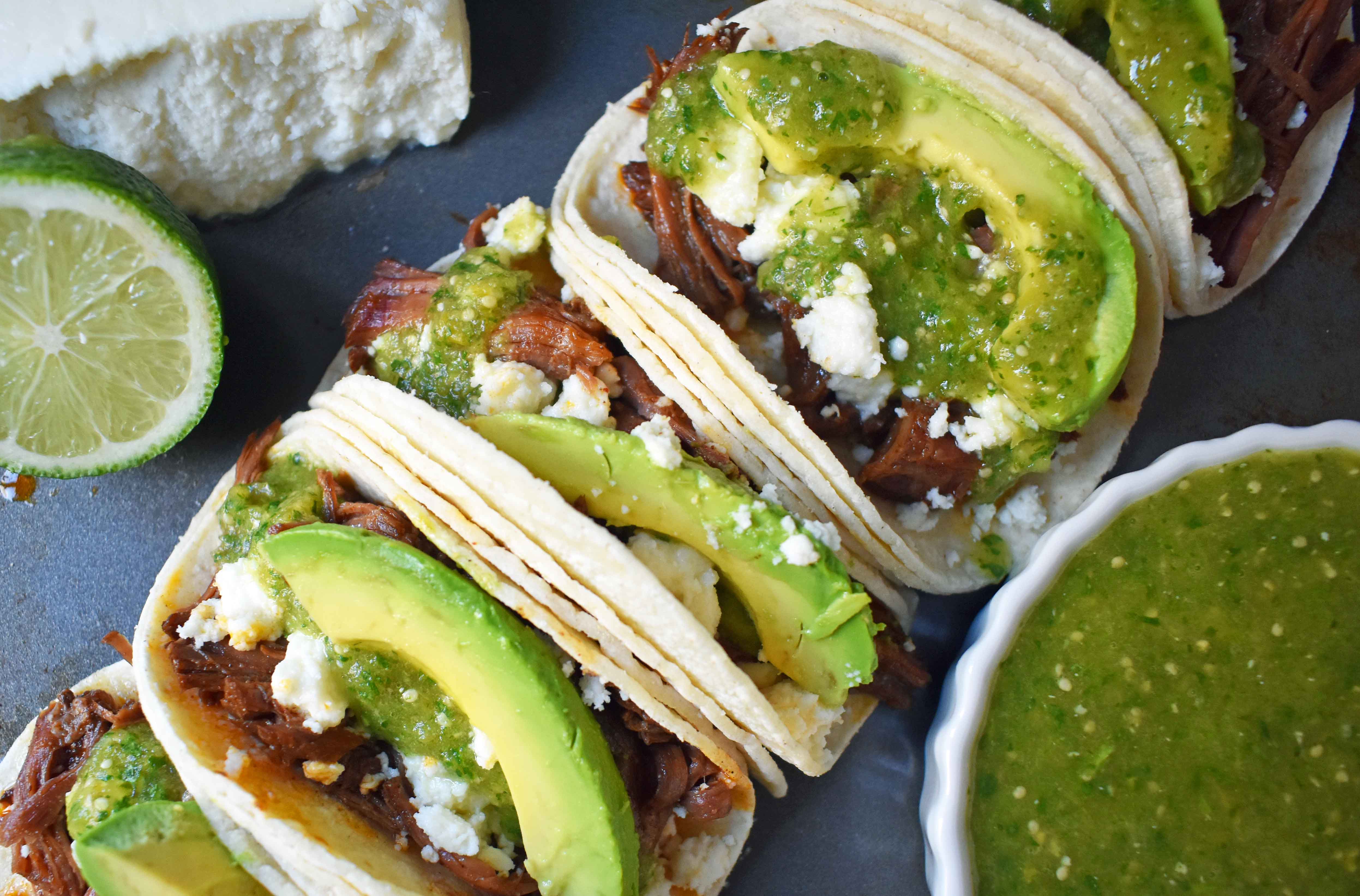 Slow Cooker Beef Barbacoa Tacos with Homemade Tomatillo Salsa. Tender spicy beef barbacoa made in slow cooker and topped with fresh avocado, queso fresco cheese, and homemade tomatillo salsa. www.modernhoney.com