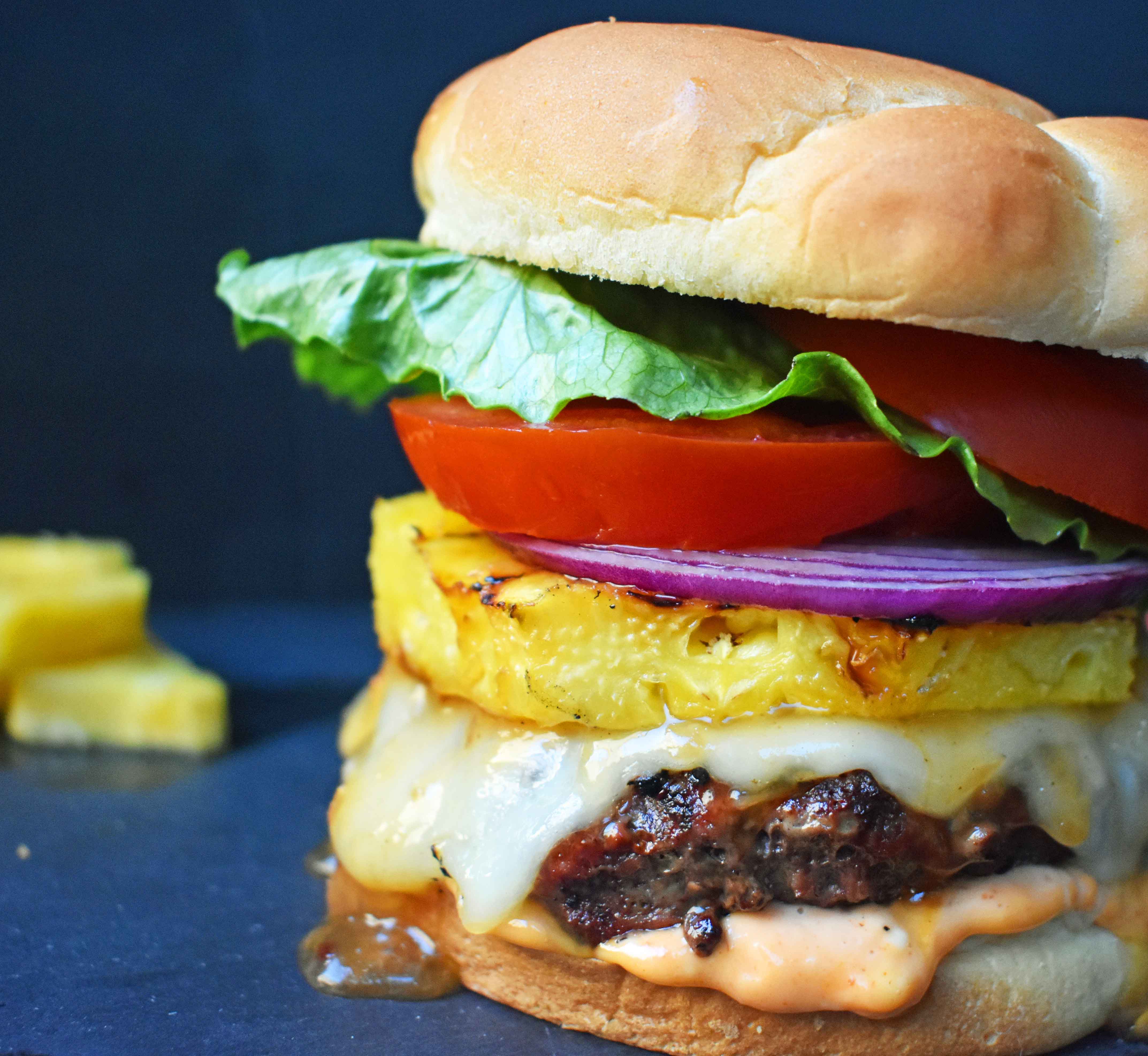 Sweet and Spicy Hawaiian Burger made with grass fed beef grilled to perfection and basted with a Hawaiian pineapple sauce and topped with melted Swiss Cheese. It is put on a warm toasted bun covered in Sriracha mayonnaise and topped with grilled pineapple, lettuce, tomato and red onion. A sweet and spicy burger that makes you think you are sitting on a beach in Hawaii! www.modernhoney.com