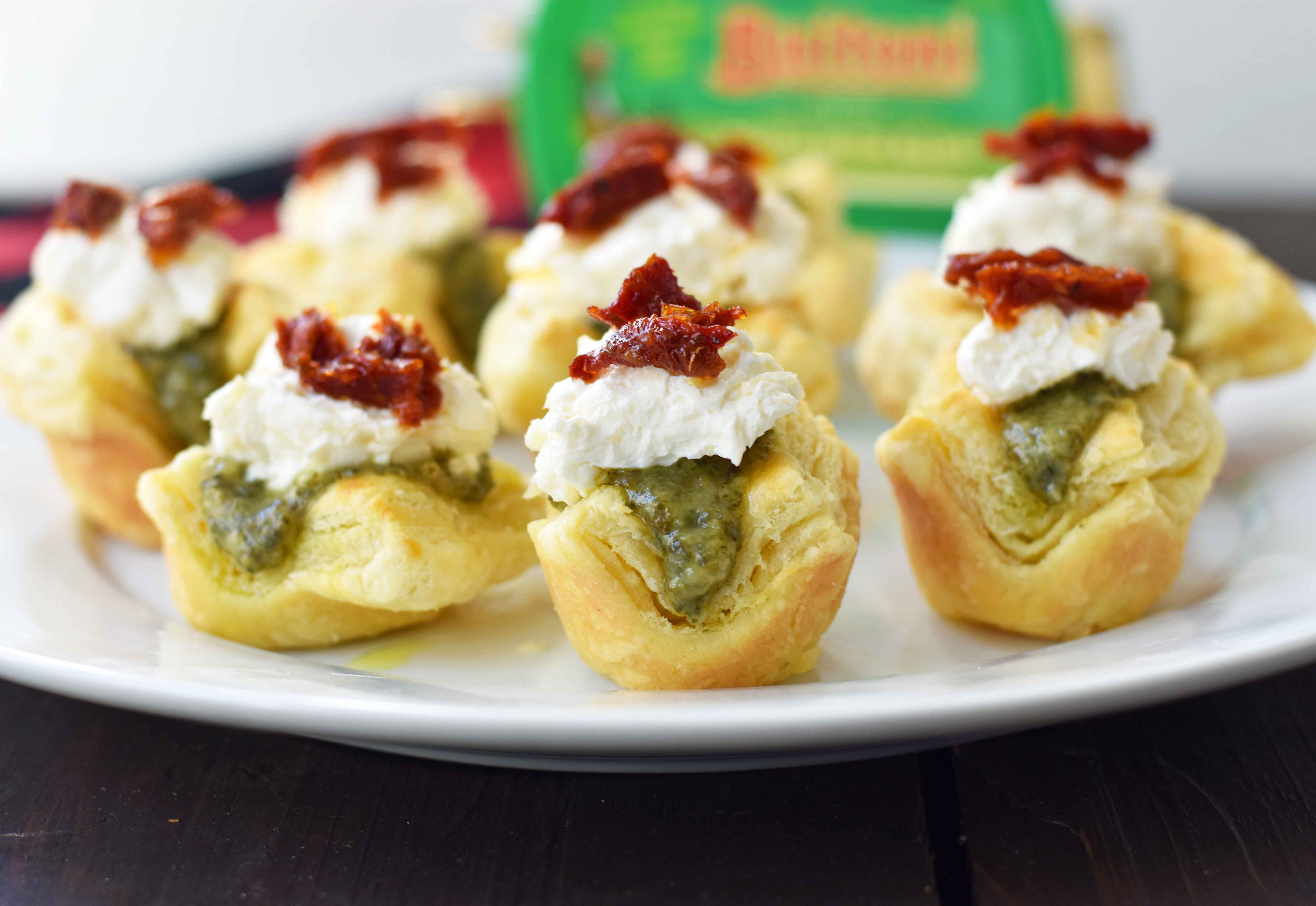 Pesto Parmesan Sundried Tomato Tartlets are made with flaky puff pastry baked until golden brown and filled with Buitoni freshly made pesto sauce, a parmesan goat cheese cream cheese layer, and topped with sweet sundried tomatoes. A beautiful and festive holiday appetizer. www.modernhoney.com @buitoniusa #sponsored 