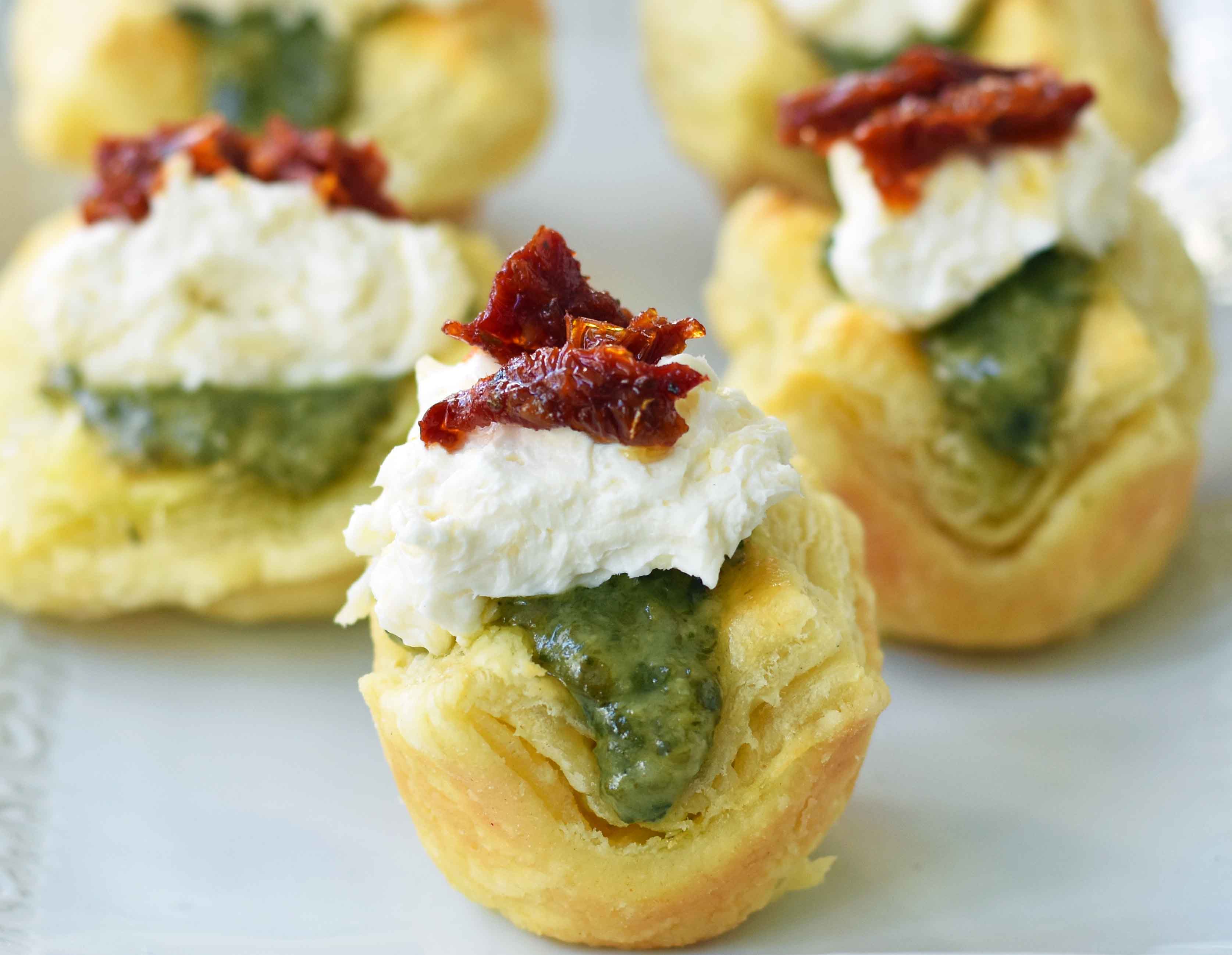 Pesto Parmesan Sundried Tomato Tartlets are made with flaky puff pastry baked until golden brown and filled with Buitoni freshly made pesto sauce, a parmesan goat cheese cream cheese layer, and topped with sweet sundried tomatoes. A beautiful and festive holiday appetizer. www.modernhoney.com @buitoniusa #sponsored