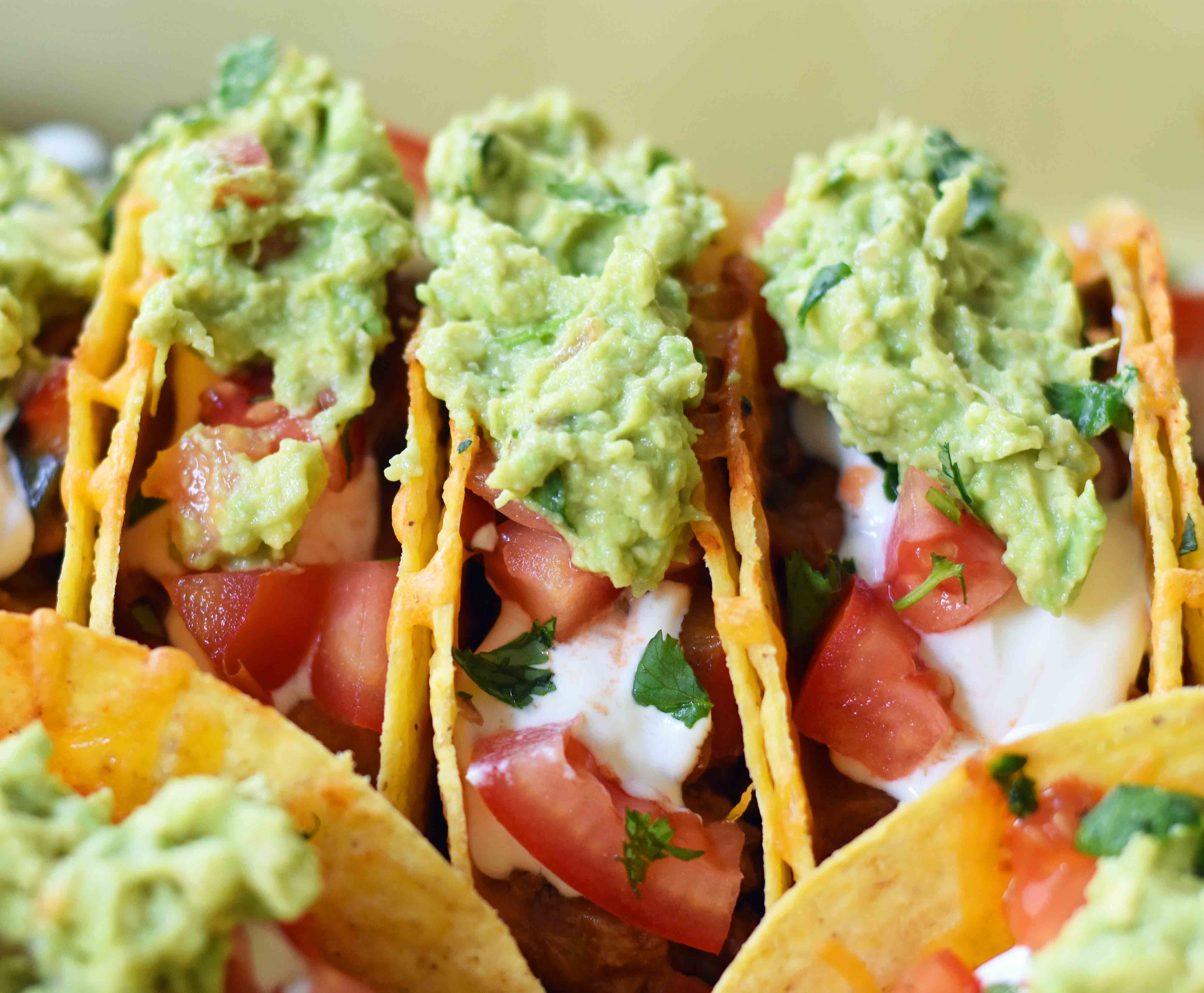 Easy Oven Baked Beef Tacos. Perfectly seasoned ground beef tacos and Mexican cheese baked in taco shells until melted. Topped with sour cream, guacamole, salsa, diced tomatoes, and hot sauce. These are party tacos and a family favorite dinner. www.modernhoney.com