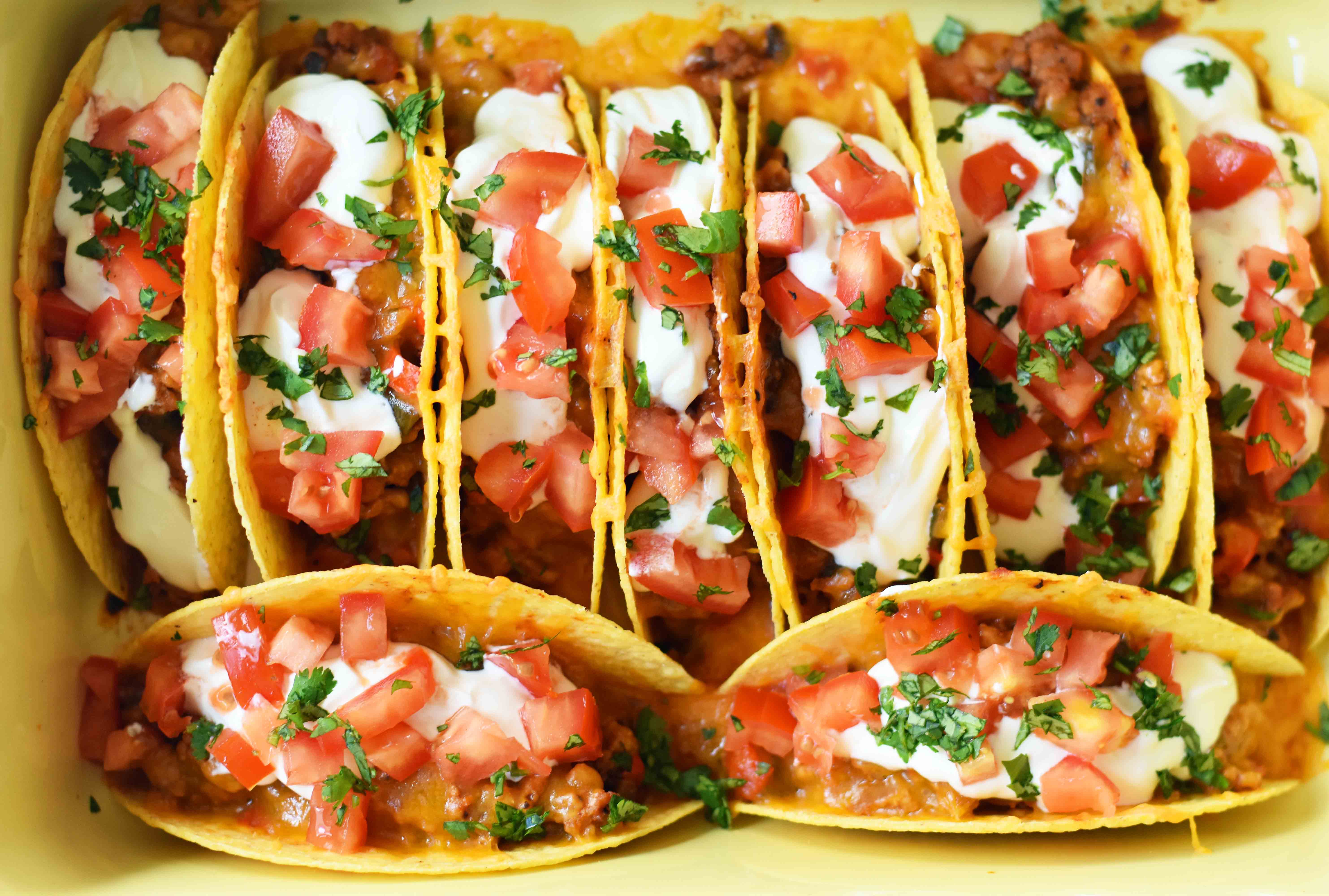 Easy Oven Baked Beef Tacos. Perfectly seasoned ground beef tacos and Mexican cheese baked in taco shells until melted. Topped with sour cream, guacamole, salsa, diced tomatoes, and hot sauce. These are party tacos and a family favorite dinner. www.modernhoney.com