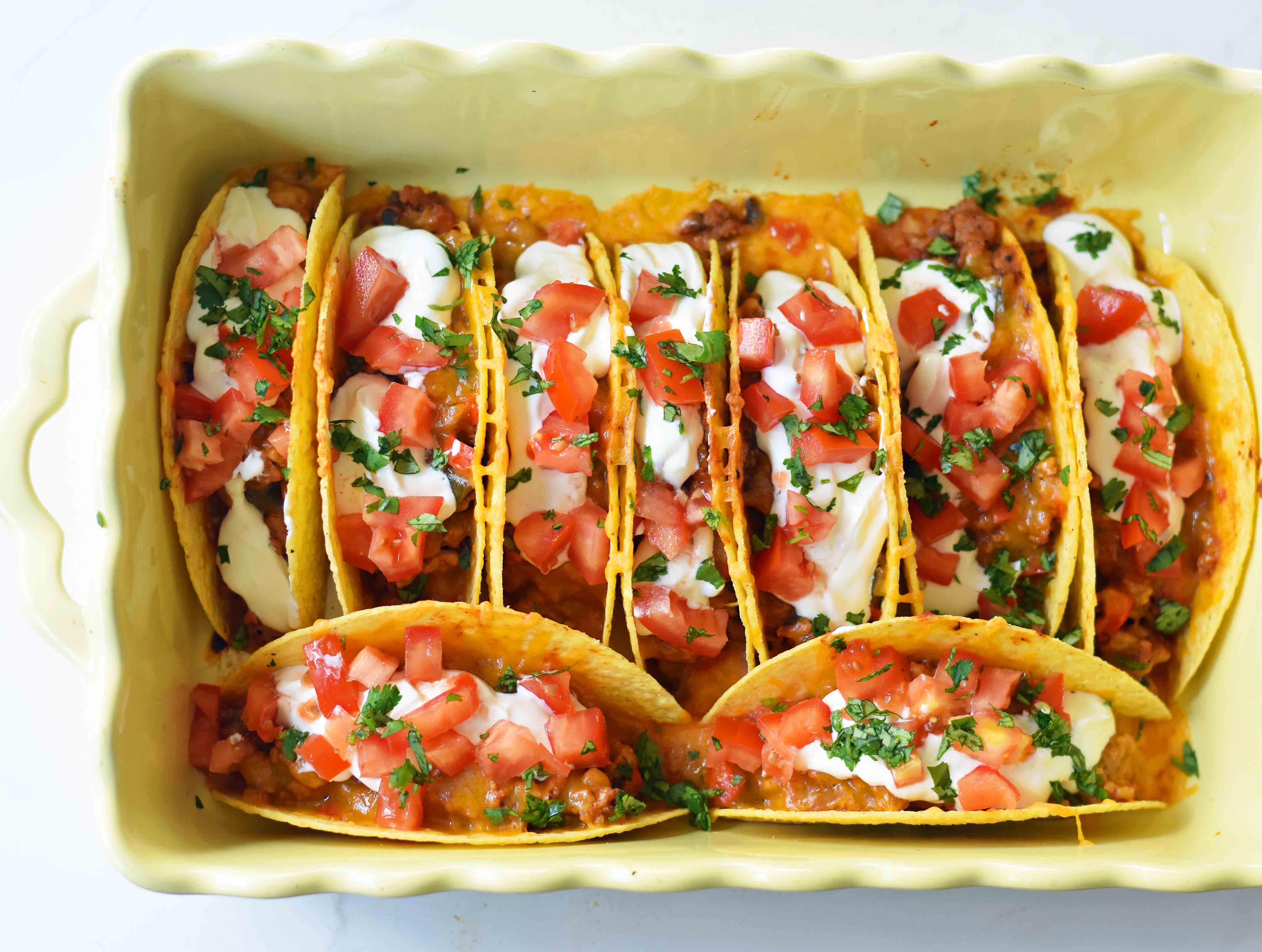 Easy Oven Baked Beef Tacos. Perfectly seasoned ground beef tacos and Mexican cheese baked in taco shells until melted. Topped with sour cream, guacamole, salsa, diced tomatoes, and hot sauce. These are party tacos and a family favorite dinner. www.modernhoney.com