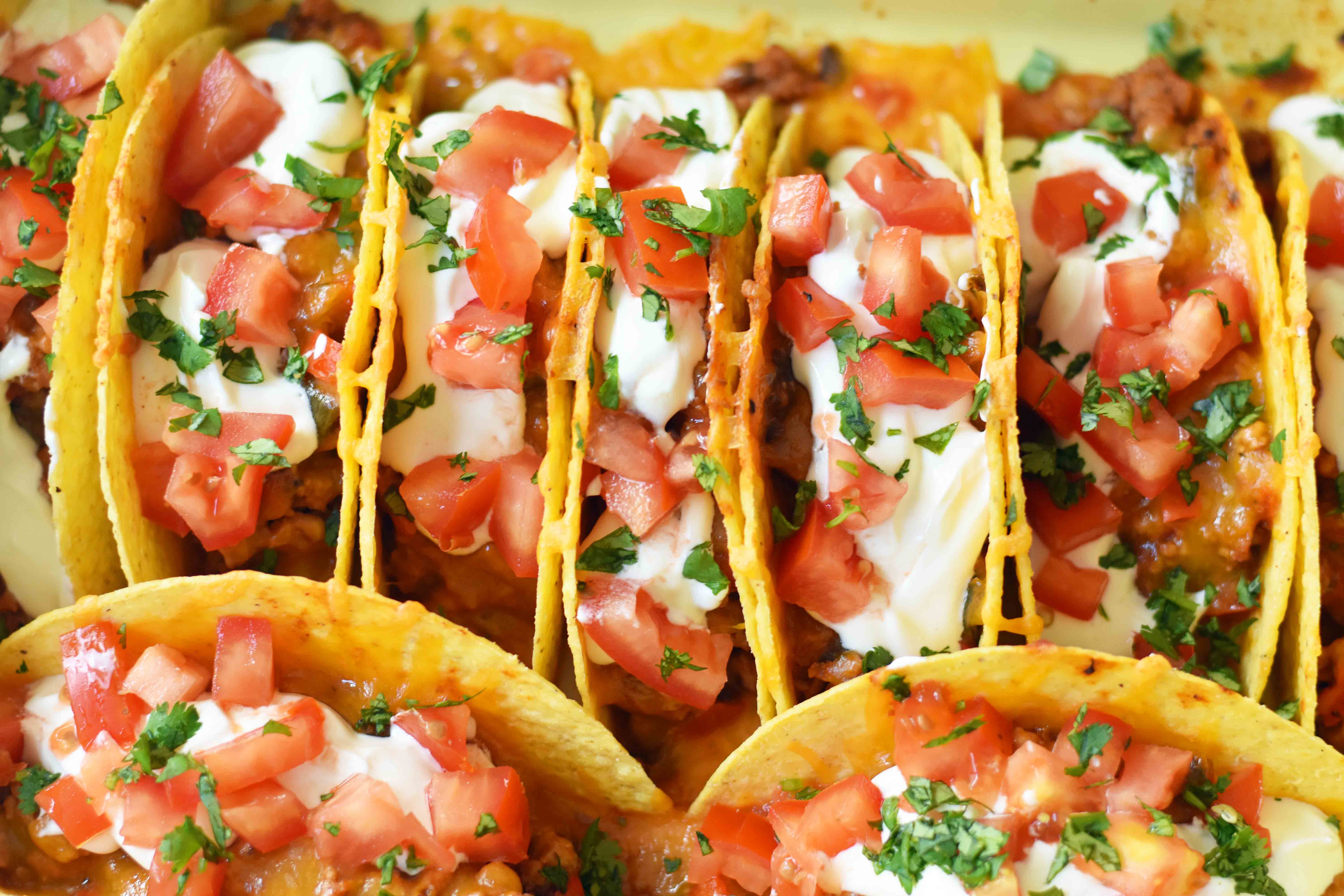 Easy Oven Baked Beef Tacos. Perfectly seasoned ground beef tacos and Mexican cheese baked in taco shells until melted. Topped with sour cream, guacamole, salsa, diced tomatoes, and hot sauce. These are party tacos and a family favorite dinner. www.modernhoney.com