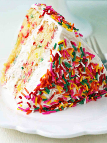 A fluffy homemade funfetti birthday cake with rainbow sprinkles topped with a light cream cheese buttercream frosting and an array of sprinkles. The perfect birthday cake! www.modernhoney.com #funfetti #funfetticake #sprinklescake #homemadefunfetticake #cake #homemadecake