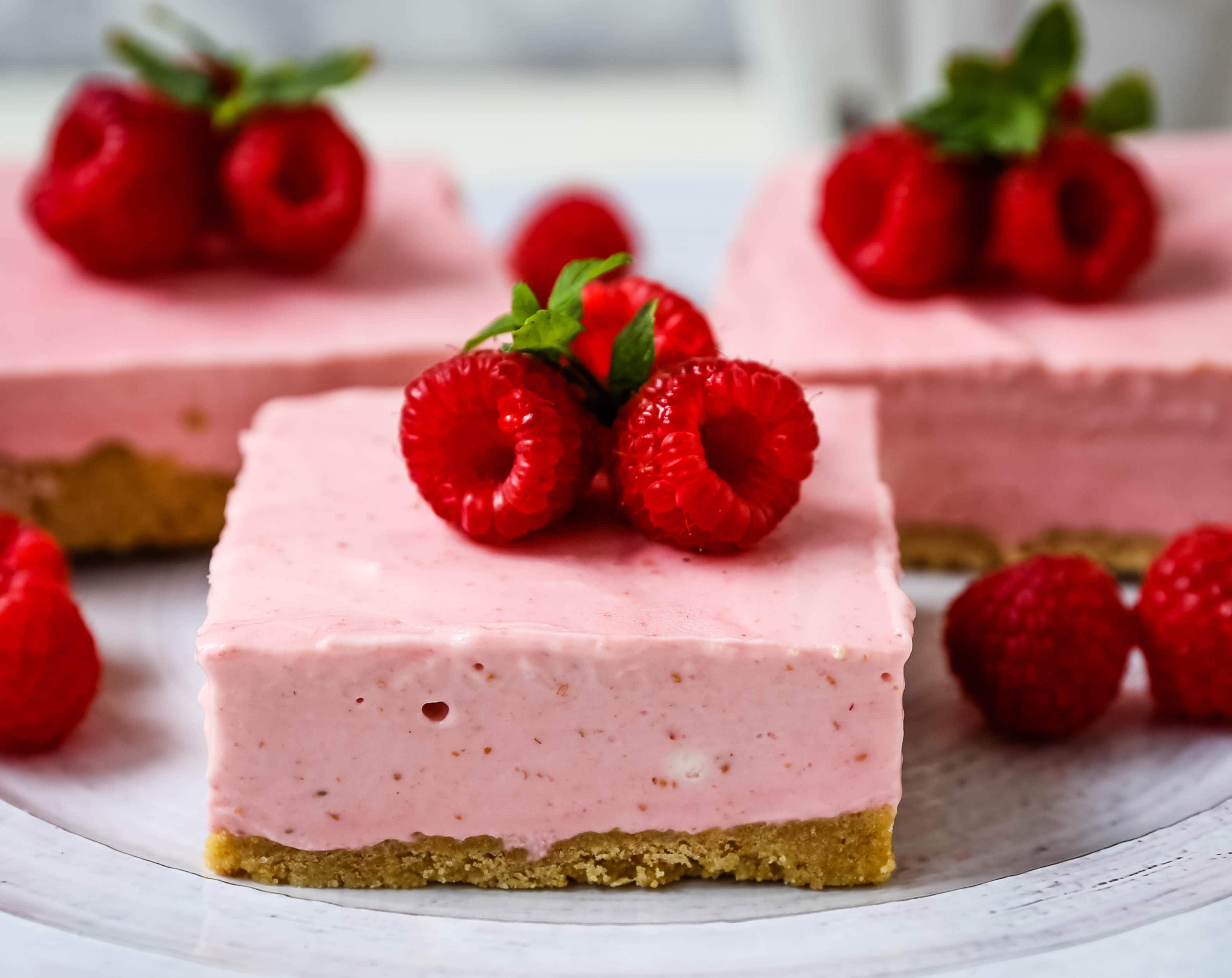 No-Bake Frozen Raspberry Cheesecake Squares. Creamy no-bake raspberry cheesecake filling on top of a shortbread or graham cracker crust topped with fresh raspberries. A creamy no-bake frozen dessert.  www.modernhoney.com #nobakedessert #raspberrycheesecake #cheesecakesquares #frozendessert #frozencheesecake