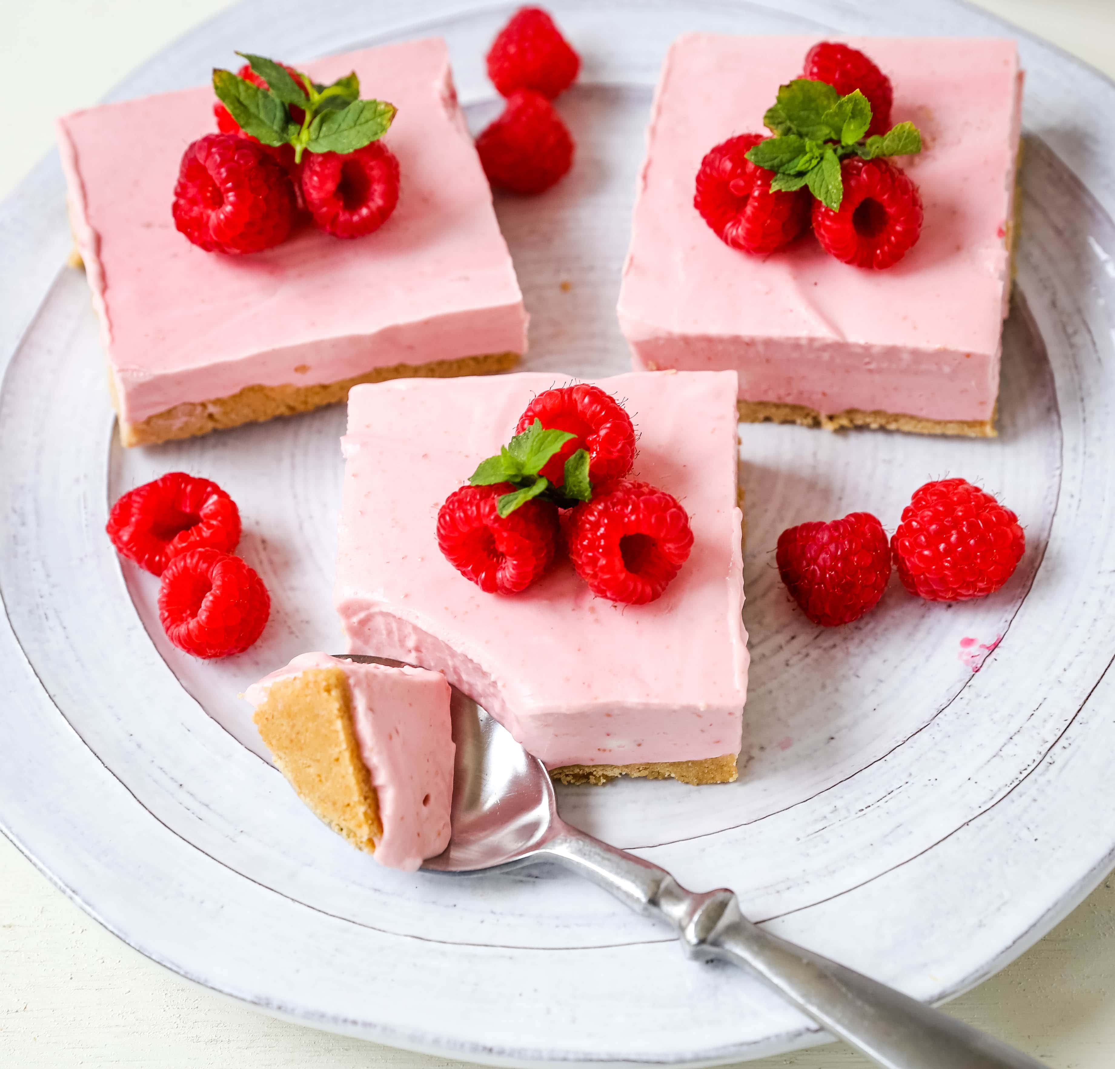 No-Bake Frozen Raspberry Cheesecake Squares. Creamy no-bake raspberry cheesecake filling on top of a shortbread or graham cracker crust topped with fresh raspberries. A creamy no-bake frozen dessert.  www.modernhoney.com #nobakedessert #raspberrycheesecake #cheesecakesquares #frozendessert #frozencheesecake