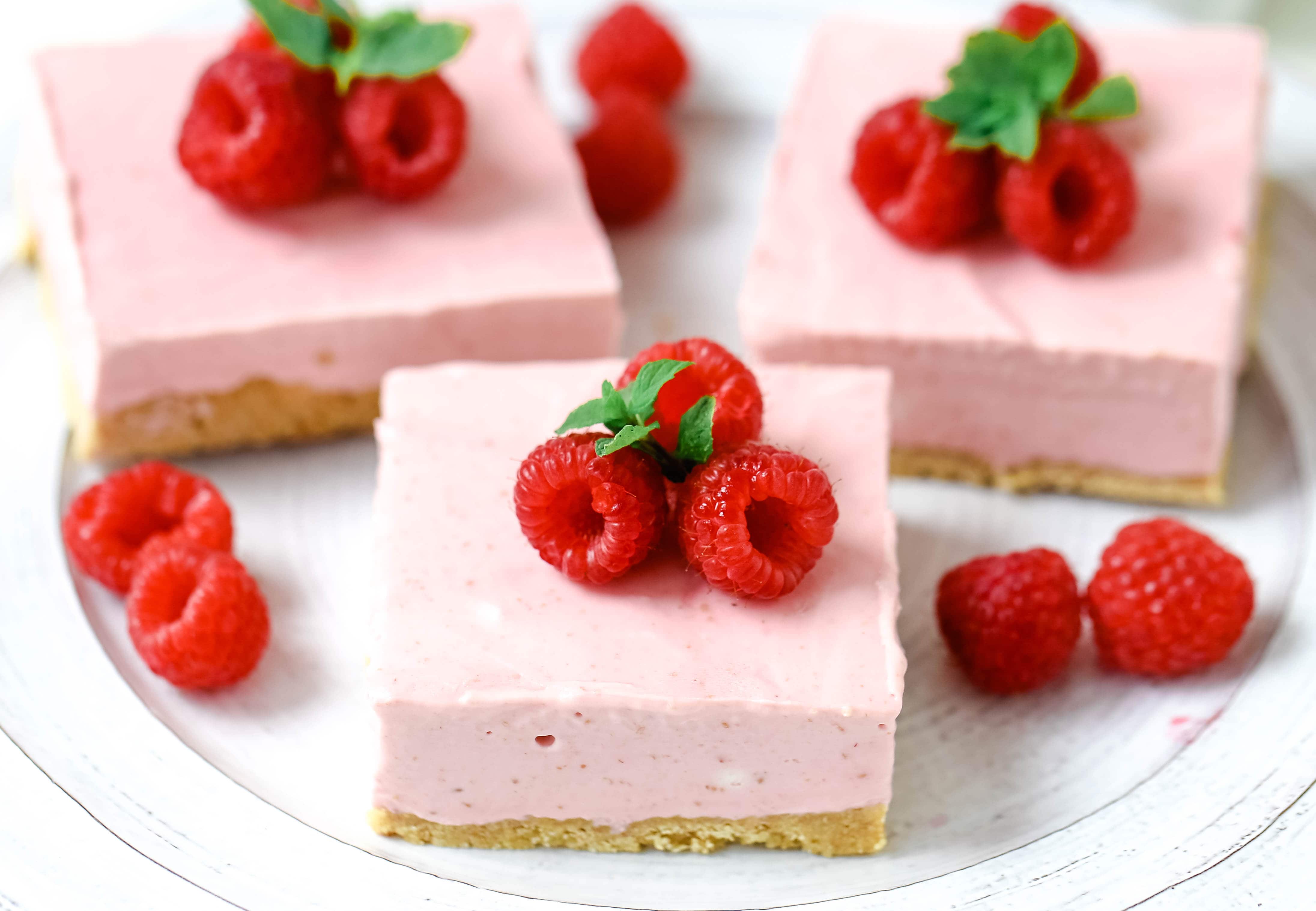 No-Bake Frozen Raspberry Cheesecake Squares. Creamy no-bake raspberry cheesecake filling on top of a shortbread or graham cracker crust topped with fresh raspberries. A creamy no-bake frozen dessert.  www.modernhoney.com #nobakedessert #raspberrycheesecake #cheesecakesquares #frozendessert #frozencheesecake