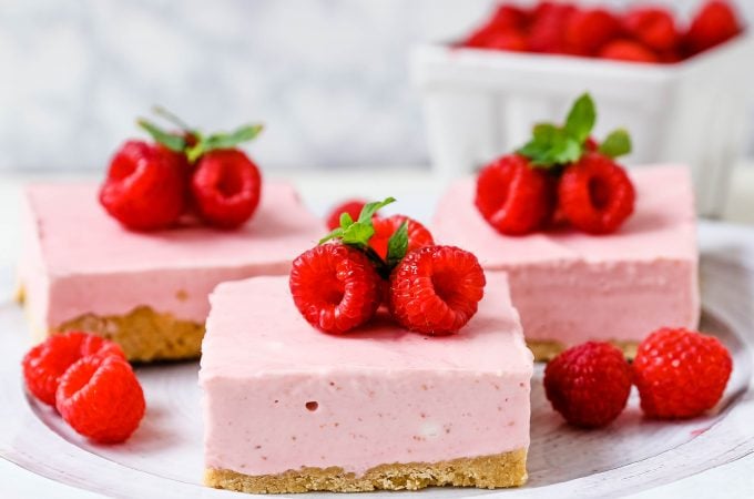 No-Bake Frozen Raspberry Cheesecake Squares. Creamy no-bake raspberry cheesecake filling on top of a shortbread or graham cracker crust topped with fresh raspberries. A creamy no-bake frozen dessert. www.modernhoney.com #nobakedessert #raspberrycheesecake #cheesecakesquares #frozendessert #frozencheesecake