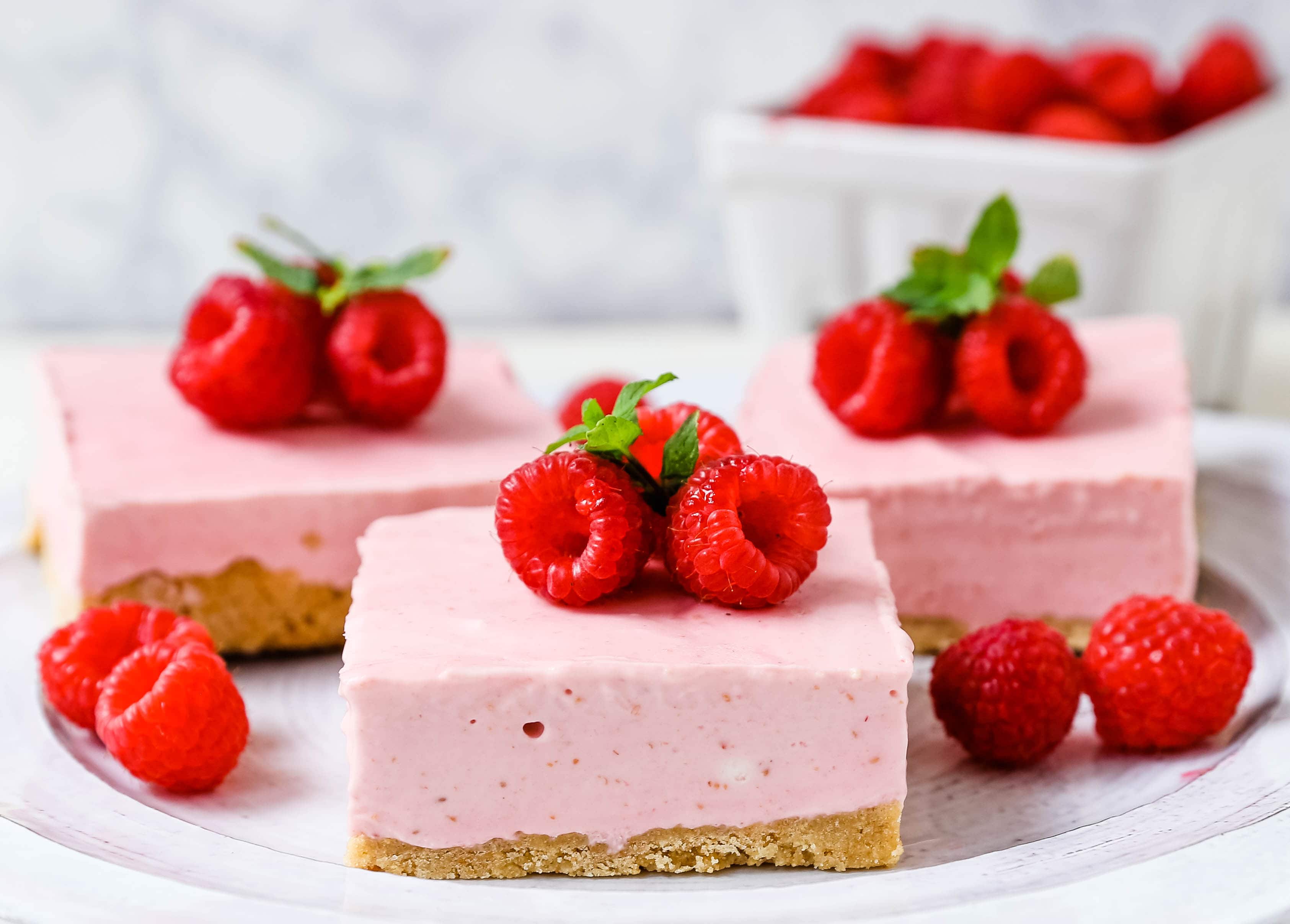 No-Bake Frozen Raspberry Cheesecake Squares. Creamy no-bake raspberry cheesecake filling on top of a shortbread or graham cracker crust topped with fresh raspberries. A creamy no-bake frozen dessert.  www.modernhoney.com #nobakedessert #raspberrycheesecake #cheesecakesquares #frozendessert #frozencheesecake