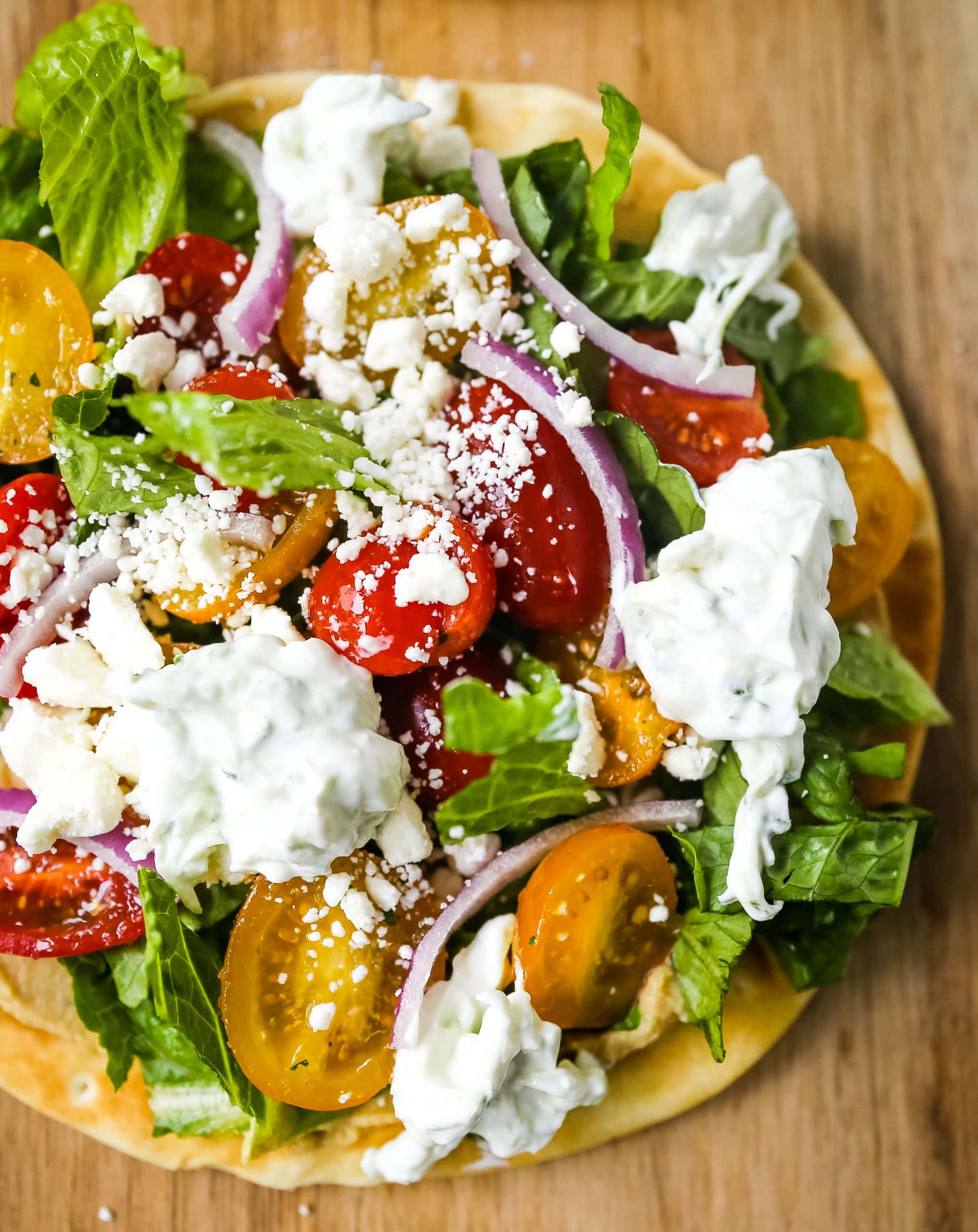 Greek Salad Pita Pizzas Soft pita bread topped with creamy hummus, romaine lettuce, juicy grape tomatoes, feta cheese, red onion, cucumber, and a homemade fresh tzatziki sauce. www.modernhoney.com #greek #greekfood #salad #pita 