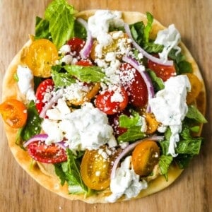 Greek Salad Pita Pizzas Soft pita bread topped with creamy hummus, romaine lettuce, juicy grape tomatoes, feta cheese, red onion, cucumber, and a homemade fresh tzatziki sauce. www.modernhoney.com #greek #greekfood #salad #pita