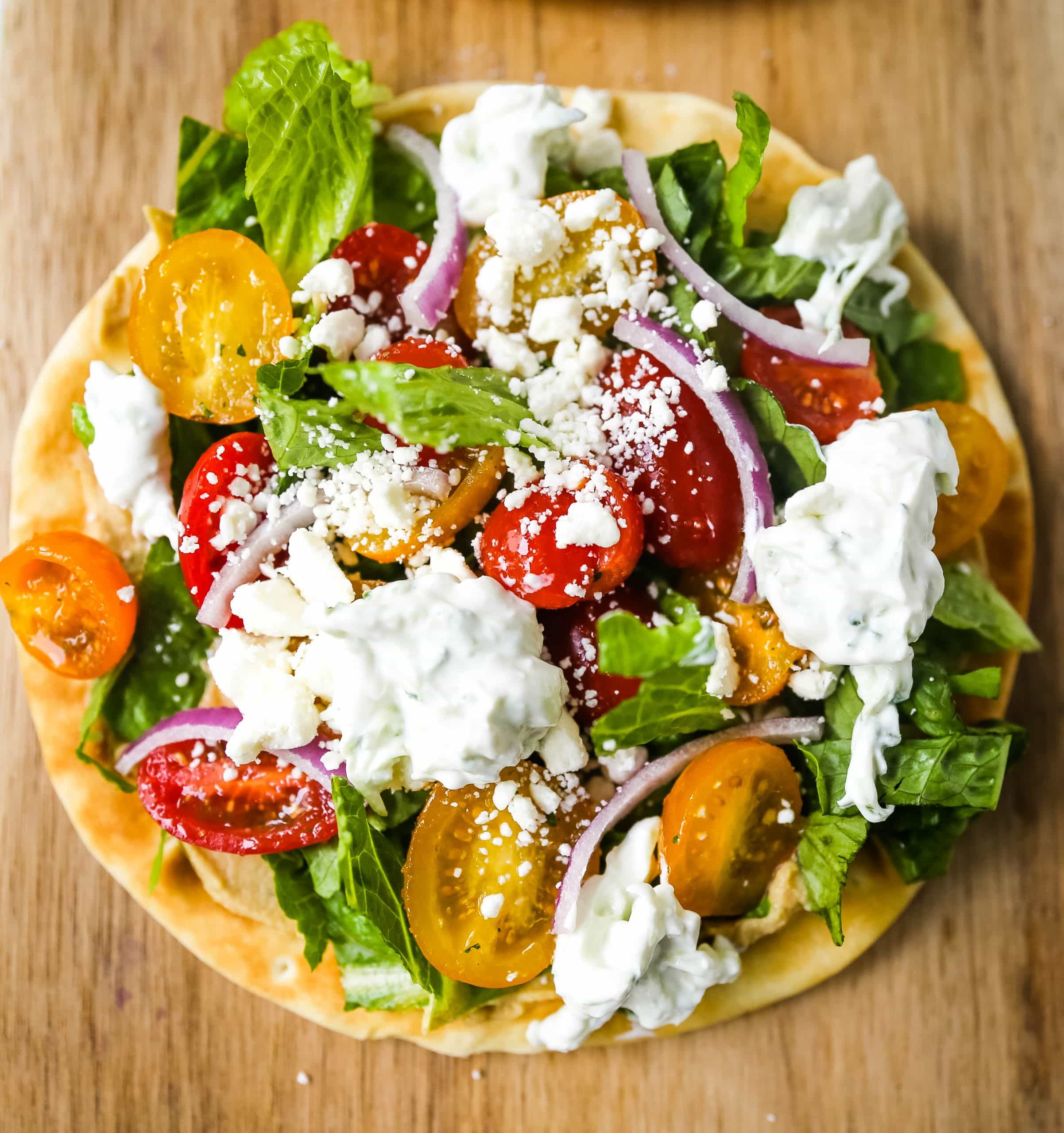 Greek Salad Pita Pizzas Soft pita bread topped with creamy hummus, romaine lettuce, juicy grape tomatoes, feta cheese, red onion, cucumber, and a homemade fresh tzatziki sauce. www.modernhoney.com #greek #greekfood #salad #pita 
