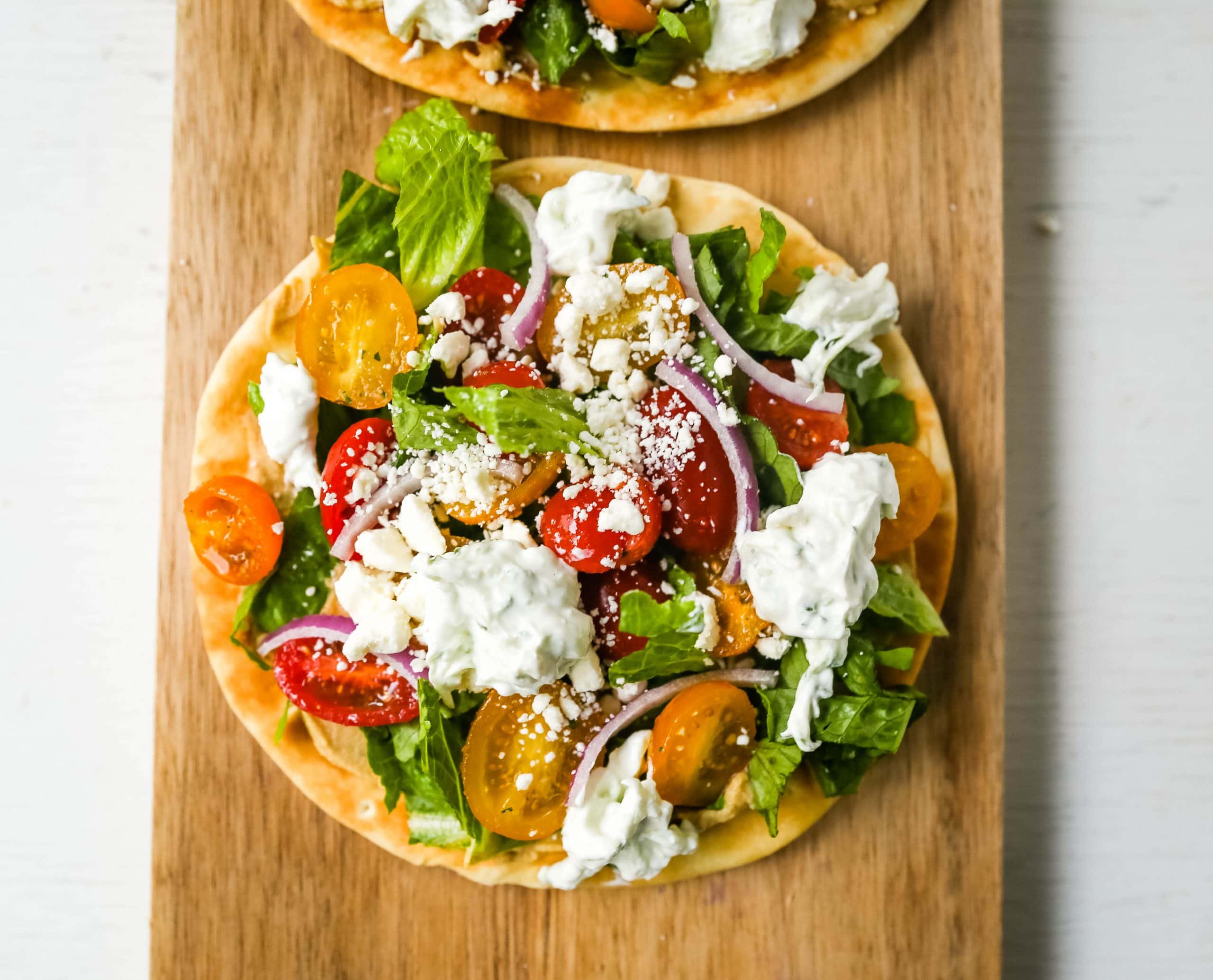 Greek Salad Pita Pizzas Soft pita bread topped with creamy hummus, romaine lettuce, juicy grape tomatoes, feta cheese, red onion, cucumber, and a homemade fresh tzatziki sauce. www.modernhoney.com #greek #greekfood #salad #pita 