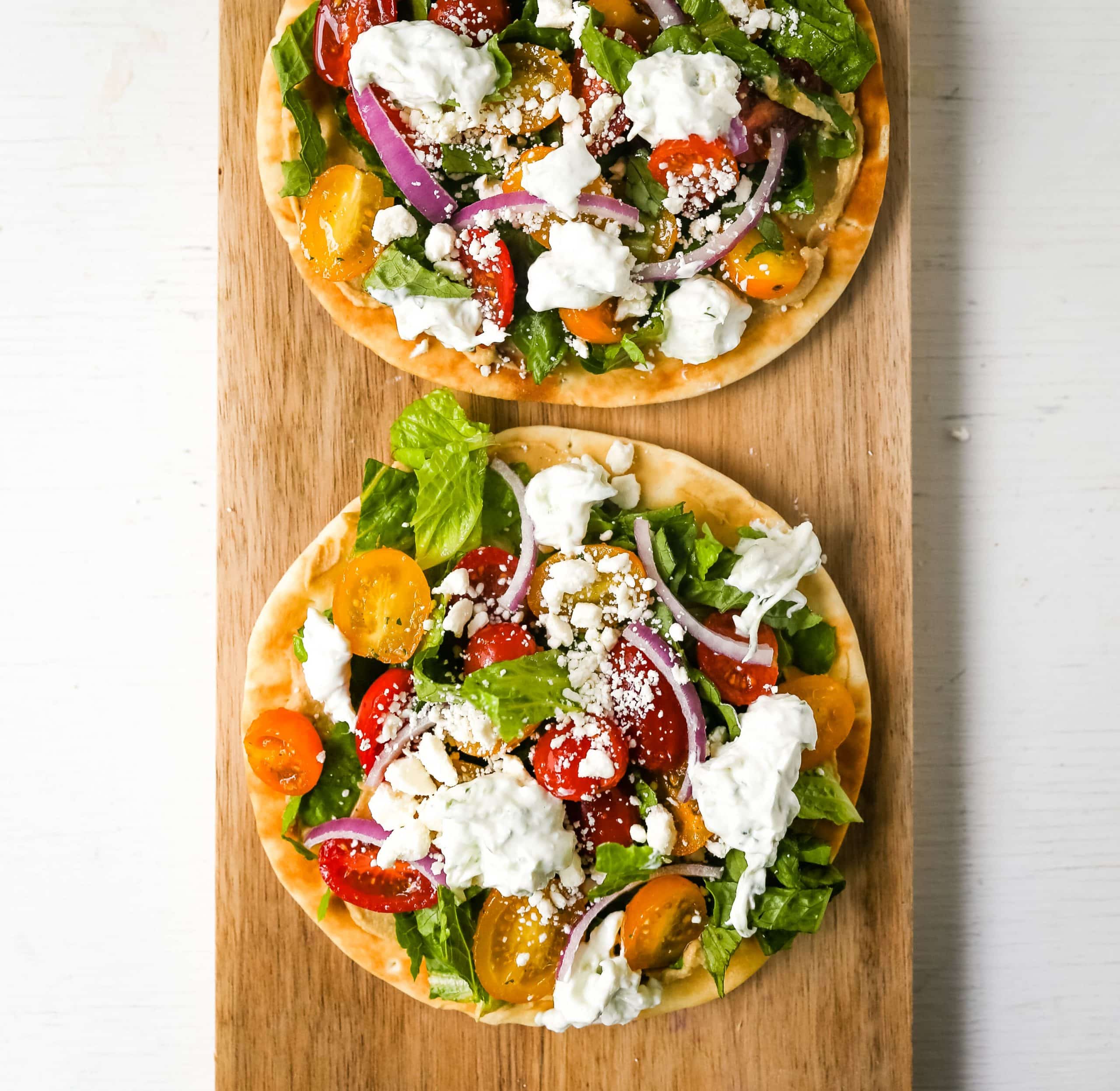 Greek Salad Pita Pizzas Soft pita bread topped with creamy hummus, romaine lettuce, juicy grape tomatoes, feta cheese, red onion, cucumber, and a homemade fresh tzatziki sauce. www.modernhoney.com #greek #greekfood #salad #pita 