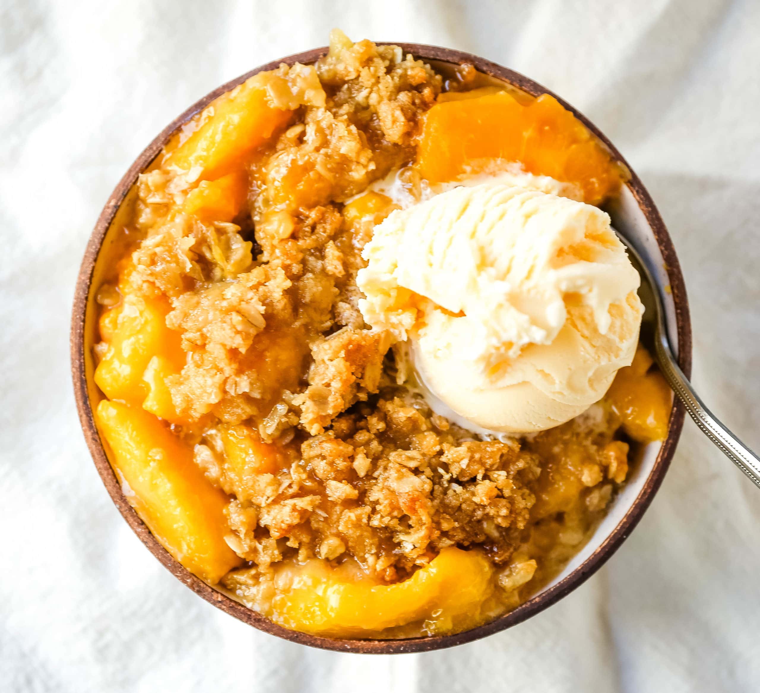 Peach Crisp. Fresh sweetened peaches with a brown sugar oat crumble topping with creamy vanilla ice cream. The perfect summer dessert! www.modernhoney.com #peach #peaches #peachcrisp #peachrecipes #peachdessert