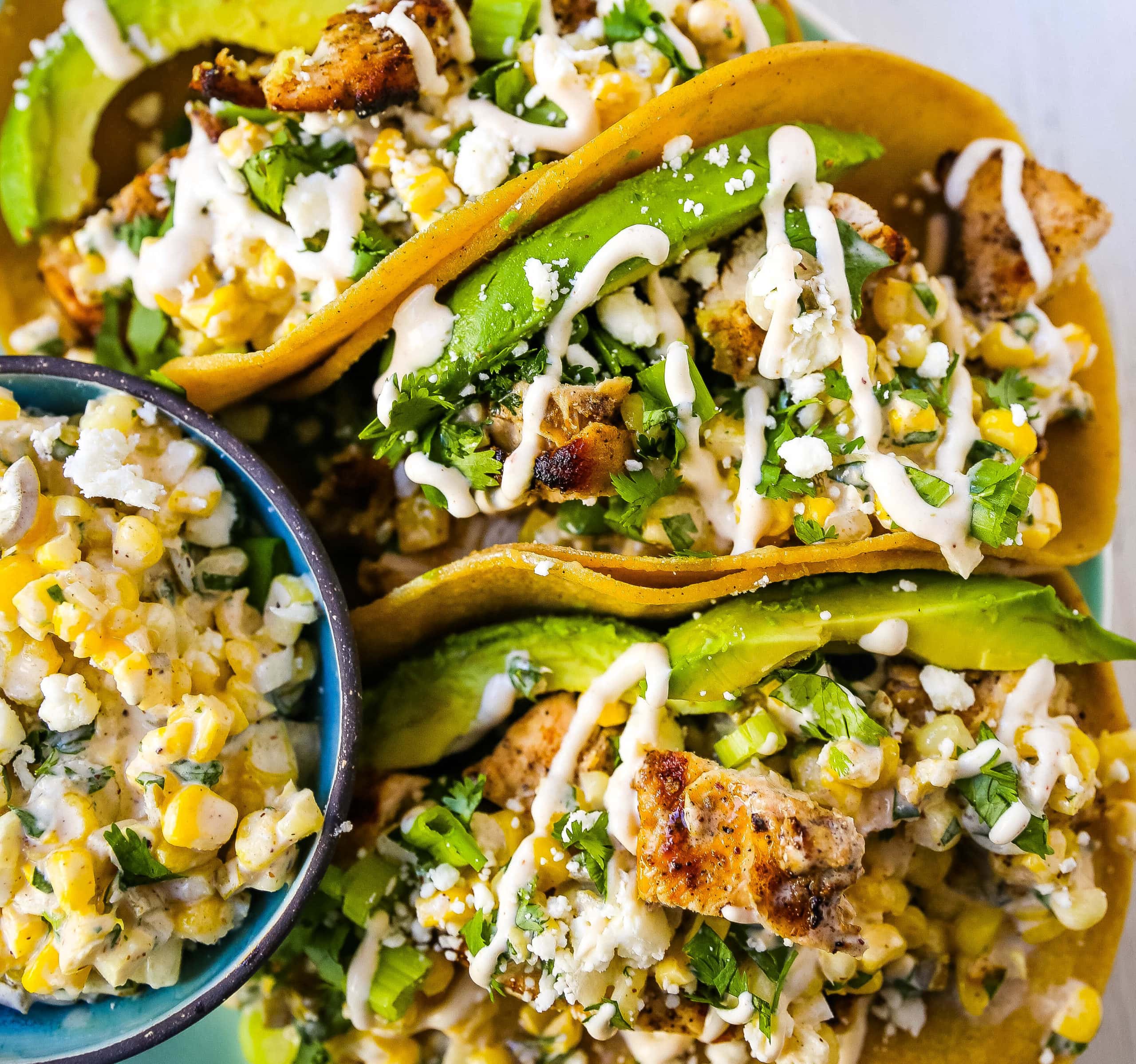 Mexican Street Corn Chicken Tacos Marinated grilled chicken with a homemade street corn salsa, fresh avocado, cotija cheese, and spiced Mexican crema. These tacos will become a family favorite in no time at all! www.modernhoney.com #taco #tacos #mexicanfood #chickentacos