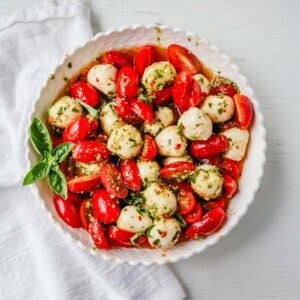 Pesto Caprese Salad. Fresh cherry or grape tomatoes, vibrant pesto sauce, creamy fresh mozzarella balls, extra-virgin olive oil, balsamic glaze, basil, and spices. A perfect summer salad recipe!