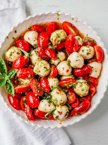 Pesto Caprese Salad. Fresh cherry or grape tomatoes, vibrant pesto sauce, creamy fresh mozzarella balls, extra-virgin olive oil, balsamic glaze, basil, and spices. A perfect summer salad recipe!