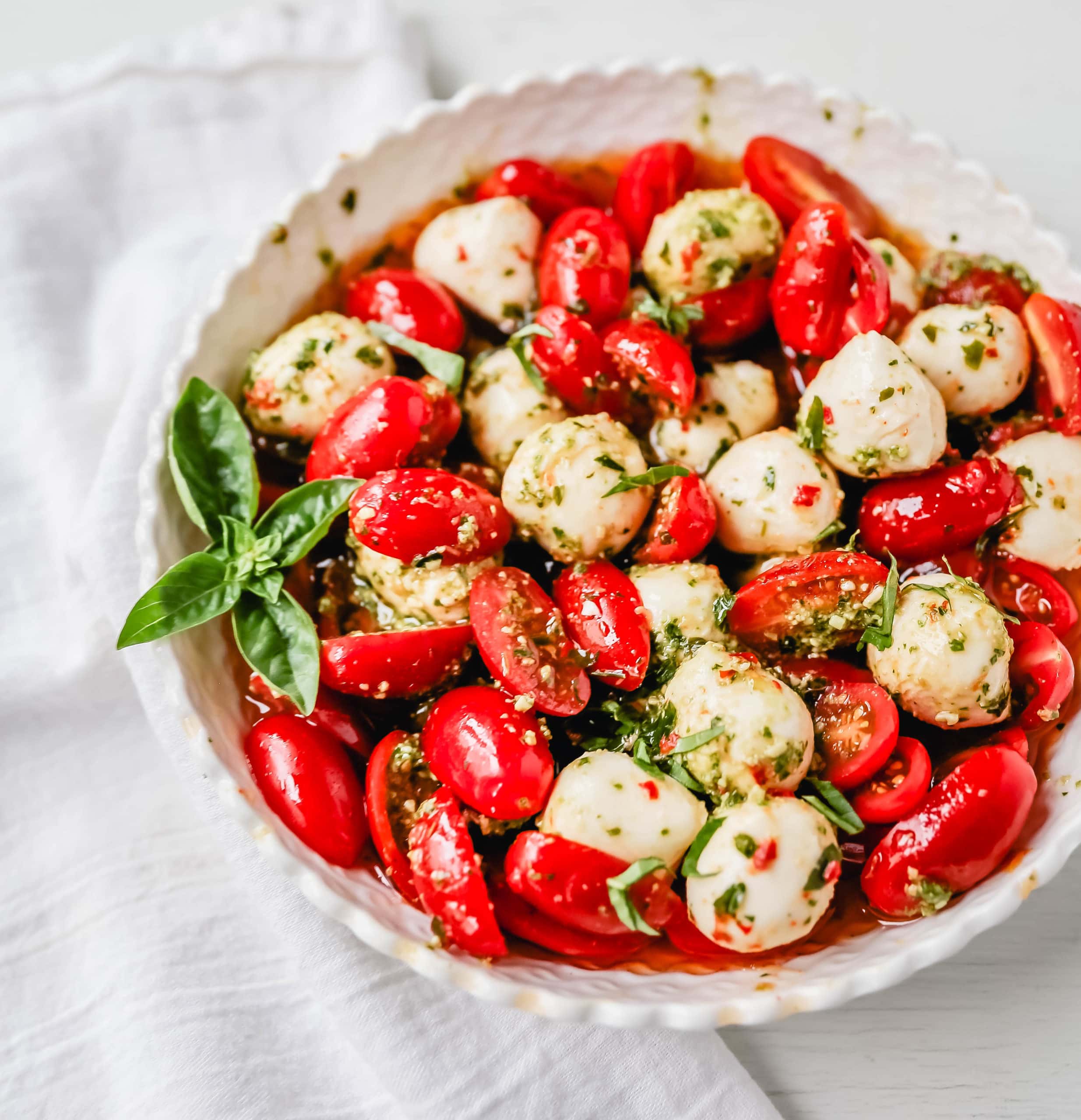 Pesto Caprese Salad. Fresh cherry or grape tomatoes, vibrant pesto sauce, creamy fresh mozzarella balls, extra-virgin olive oil, balsamic glaze, basil, and spices. A perfect summer salad recipe!