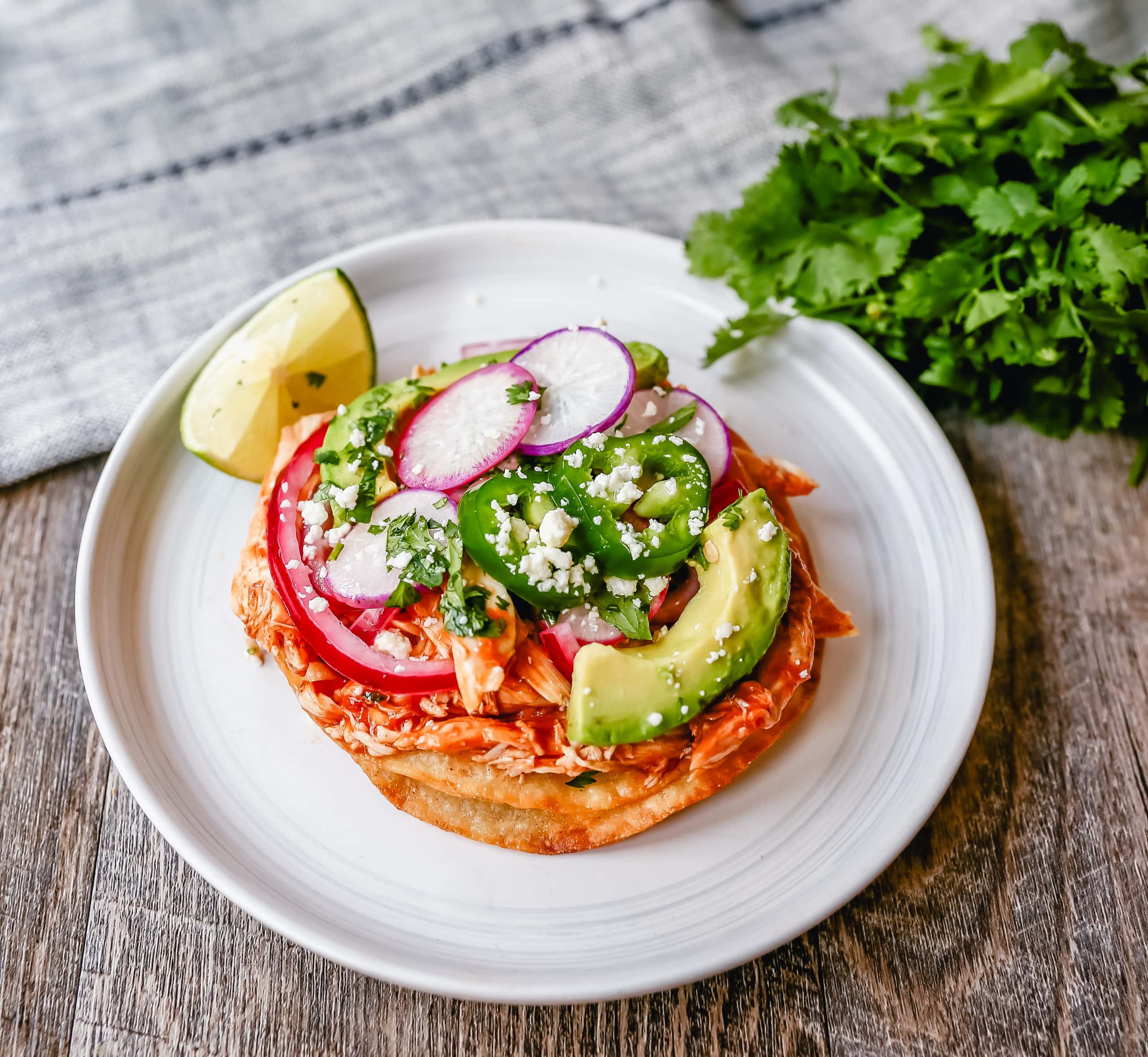 Chicken Tostadas Chile Chicken Tostadas made with homemade tostada shells topped with chile spiced chicken topped with cotija cheese, cilantro, pickled red onion, fresh avocado, and jalapeños.