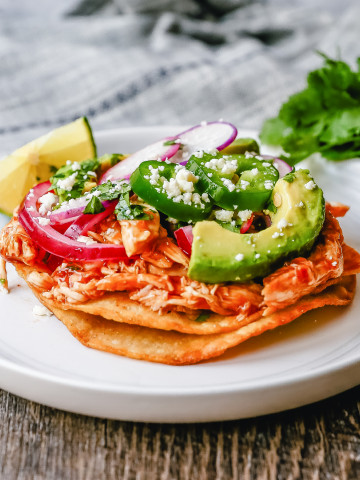 Chicken Tostadas Chile Chicken Tostadas made with homemade tostada shells topped with chile spiced chicken topped with cotija cheese, cilantro, pickled red onion, fresh avocado, and jalapeños.