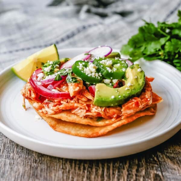 Chicken Tostadas Chile Chicken Tostadas made with homemade tostada shells topped with chile spiced chicken topped with cotija cheese, cilantro, pickled red onion, fresh avocado, and jalapeños.