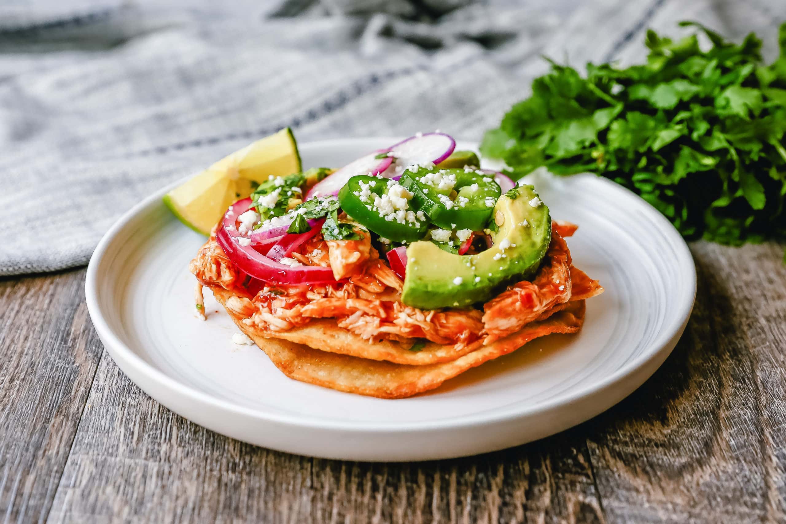 Chicken Tostadas Chile Chicken Tostadas made with homemade tostada shells topped with chile spiced chicken topped with cotija cheese, cilantro, pickled red onion, fresh avocado, and jalapeños.