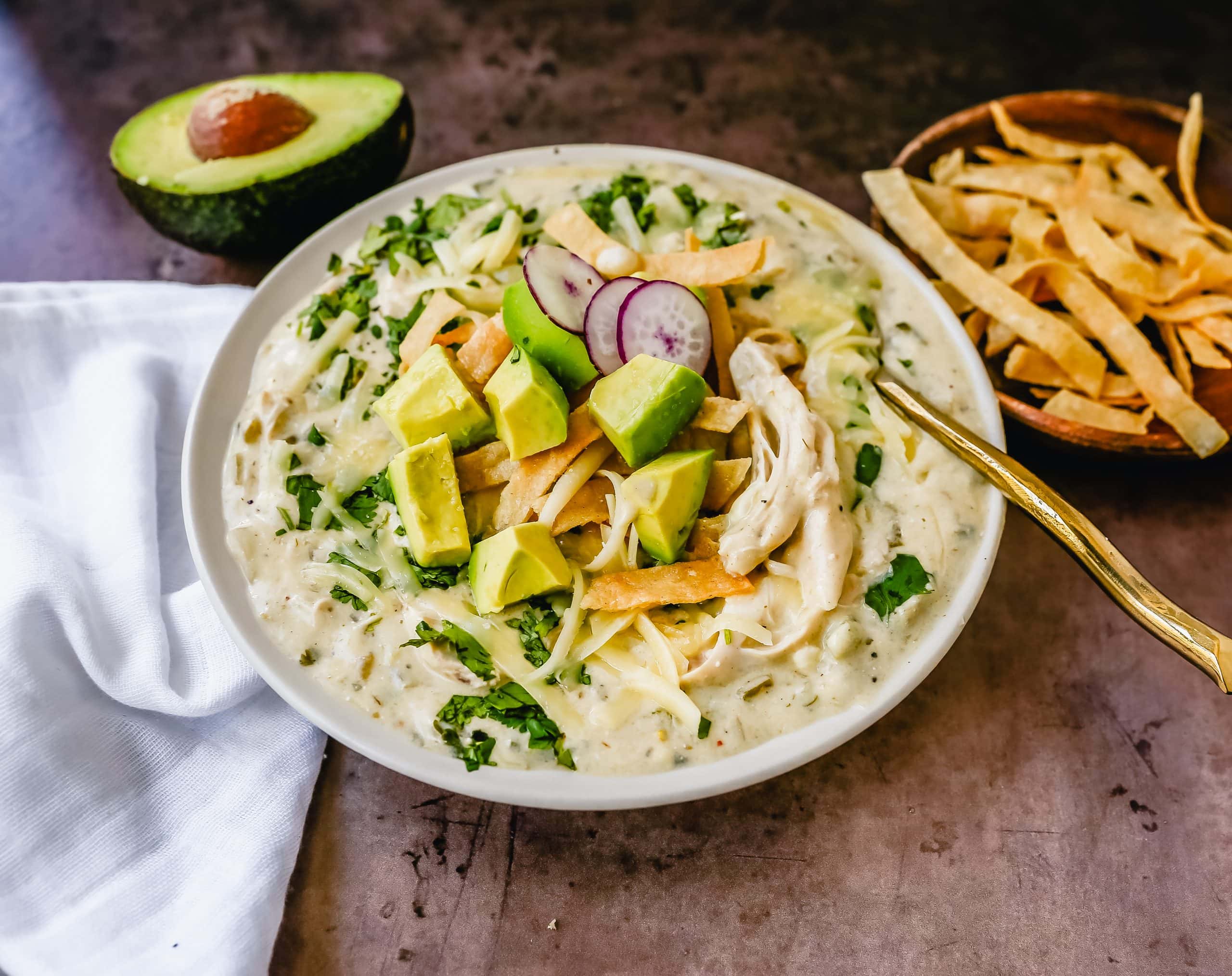 This Green Chile Chicken Enchilada Soup is made with tender chicken, green enchilada sauce, green chilies, cream cheese all in a chicken broth and topped with homemade fried tortilla strips, fresh avocado, cilantro, and Monterey Jack cheese. This is the most flavor-packed creamy green chicken enchilada soup recipe.