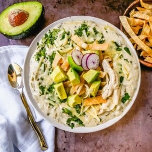 This Green Chile Chicken Enchilada Soup is made with tender chicken, green enchilada sauce, green chilies, cream cheese all in a chicken broth and topped with homemade fried tortilla strips, fresh avocado, cilantro, and Monterey Jack cheese. This is the most flavor-packed creamy green chicken enchilada soup recipe.