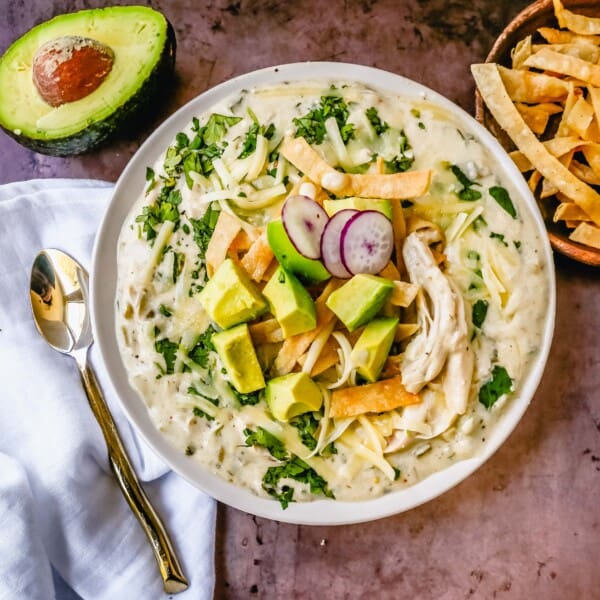 This Green Chile Chicken Enchilada Soup is made with tender chicken, green enchilada sauce, green chilies, cream cheese all in a chicken broth and topped with homemade fried tortilla strips, fresh avocado, cilantro, and Monterey Jack cheese. This is the most flavor-packed creamy green chicken enchilada soup recipe.