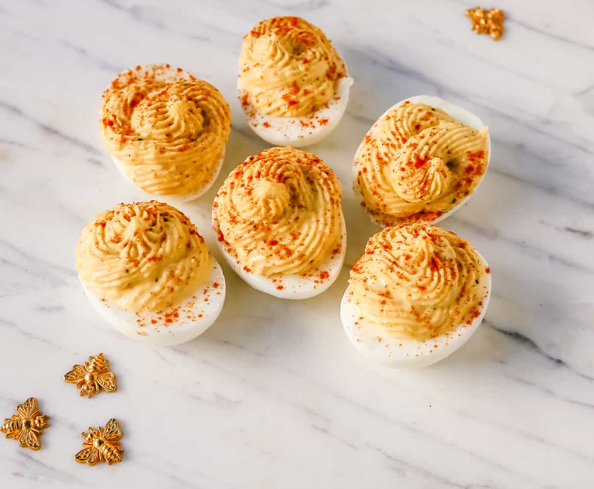 These easy deviled eggs are made with hard-boiled eggs, mayonnaise, mustard, pickle juice, a touch of sugar, a pinch of salt, and pepper, and sprinkled with paprika.