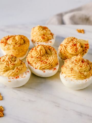 These easy deviled eggs are made with hard-boiled eggs, mayonnaise, mustard, pickle juice, a touch of sugar, a pinch of salt, and pepper, and sprinkled with paprika.