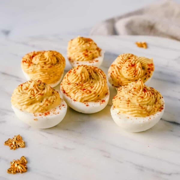 These easy deviled eggs are made with hard-boiled eggs, mayonnaise, mustard, pickle juice, a touch of sugar, a pinch of salt, and pepper, and sprinkled with paprika.